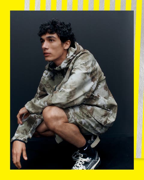 A man wearing a camo-print hoodie and shorts with sneakers.