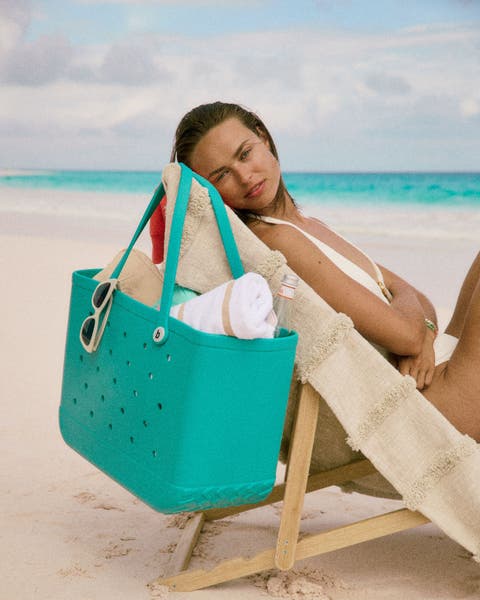 Woman at the beach with a large aqua tote and sunglasses.