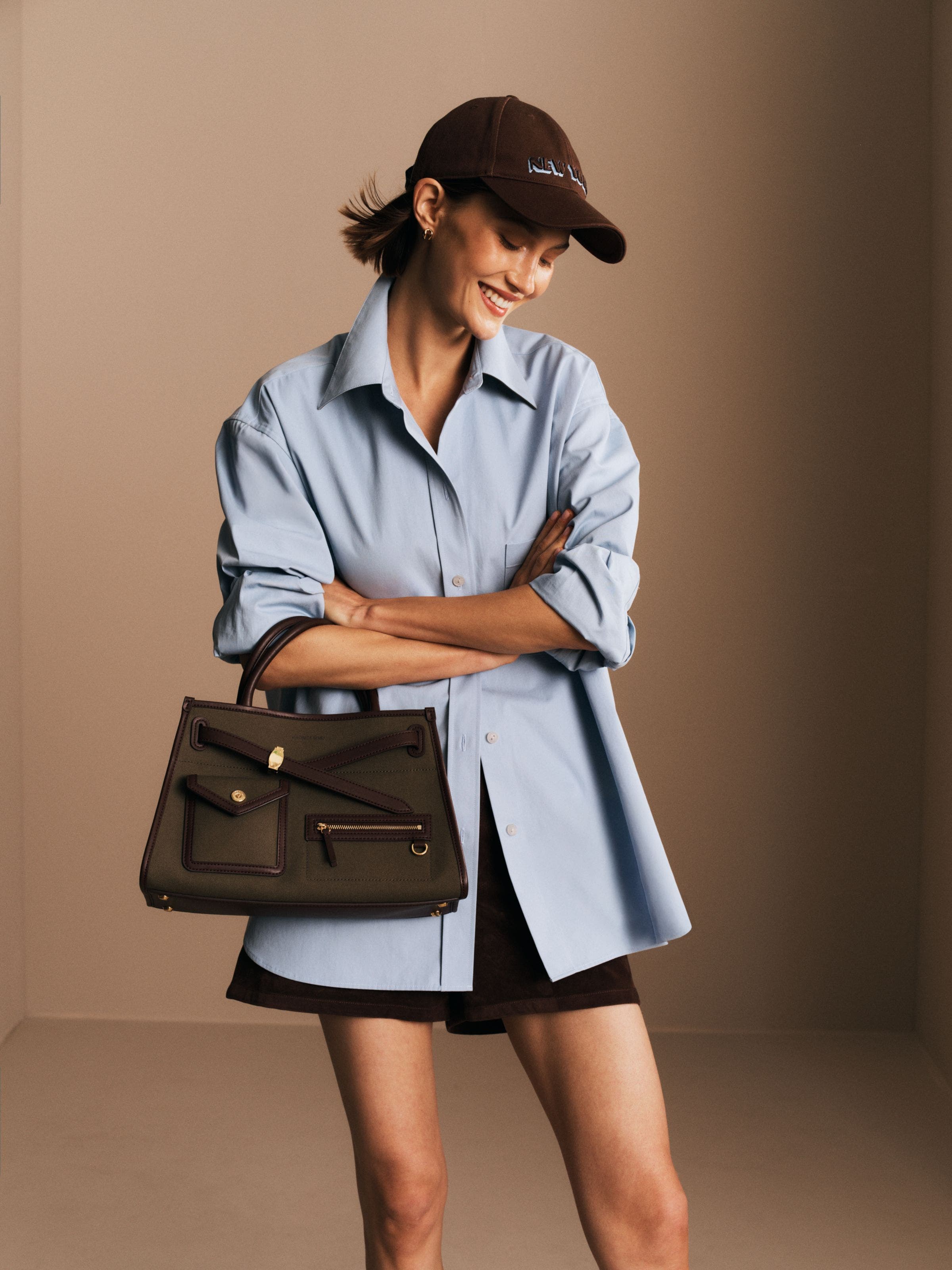 Woman in a button-down shirt, shorts and baseball cap holding a handbag.