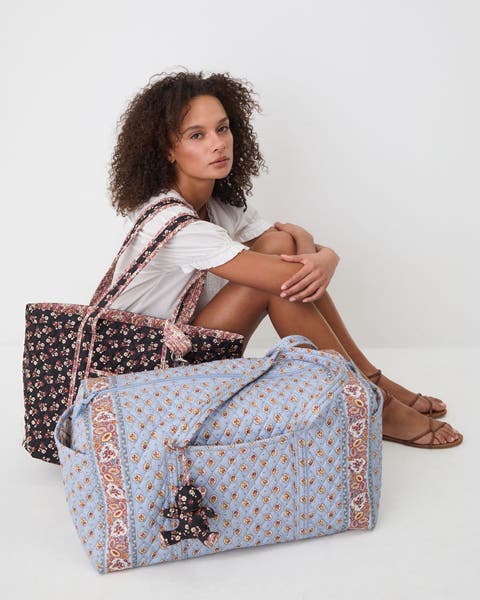 A woman sitting on the ground holding two Vera Bradley totes.