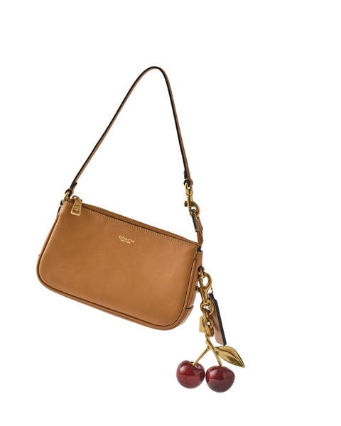 A Coach handbag with a cherry bag charm.