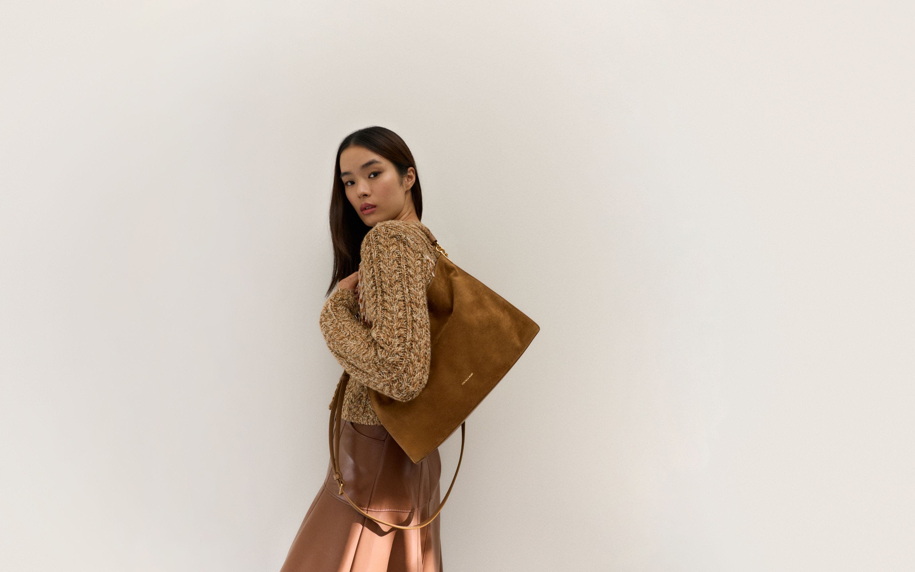 Woman wearing a sweater and skirt with a suede bag.