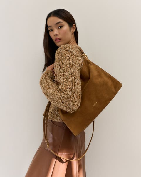 Woman wearing a sweater and skirt with a suede bag.