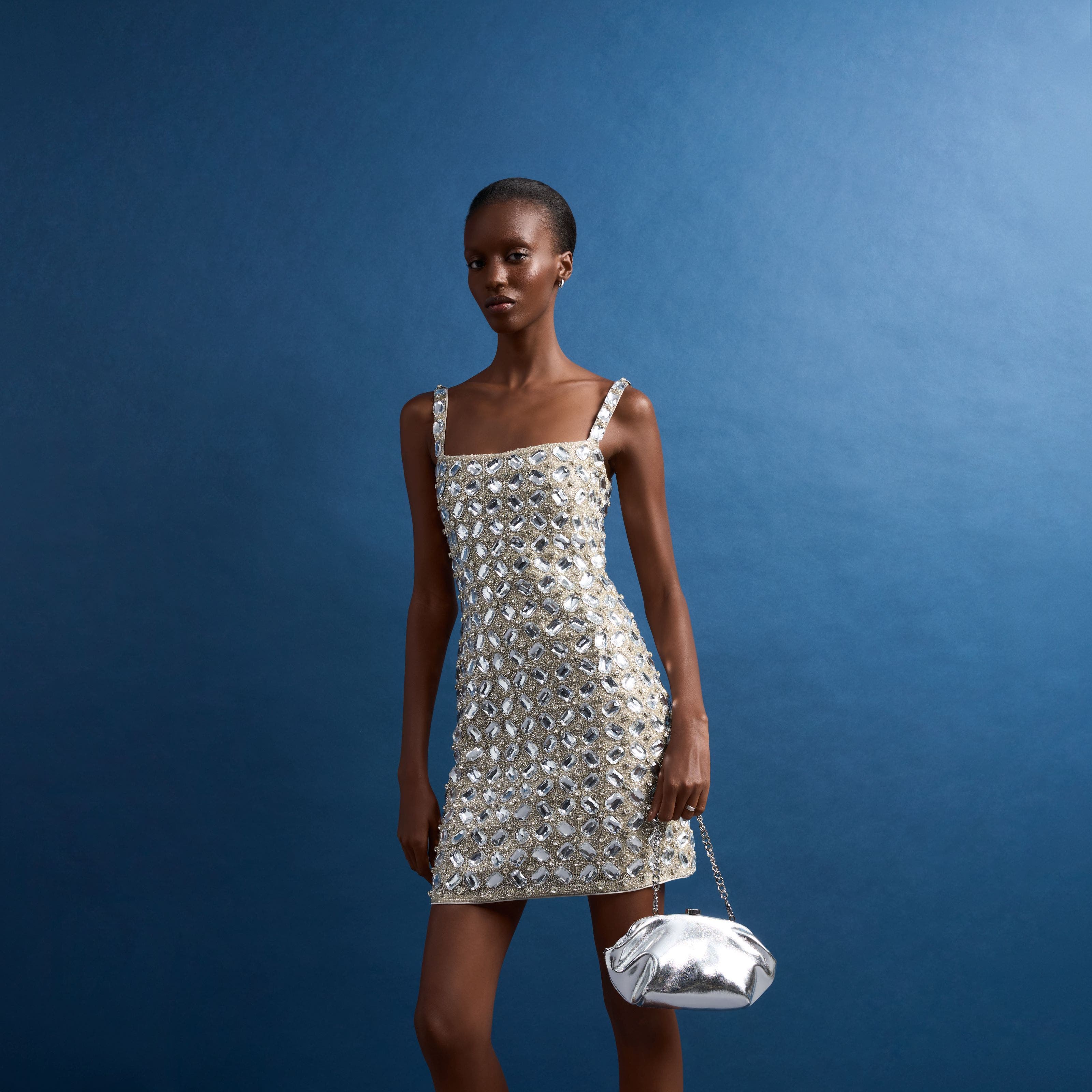 A woman in a silver embellished mini dress with a matching bag.