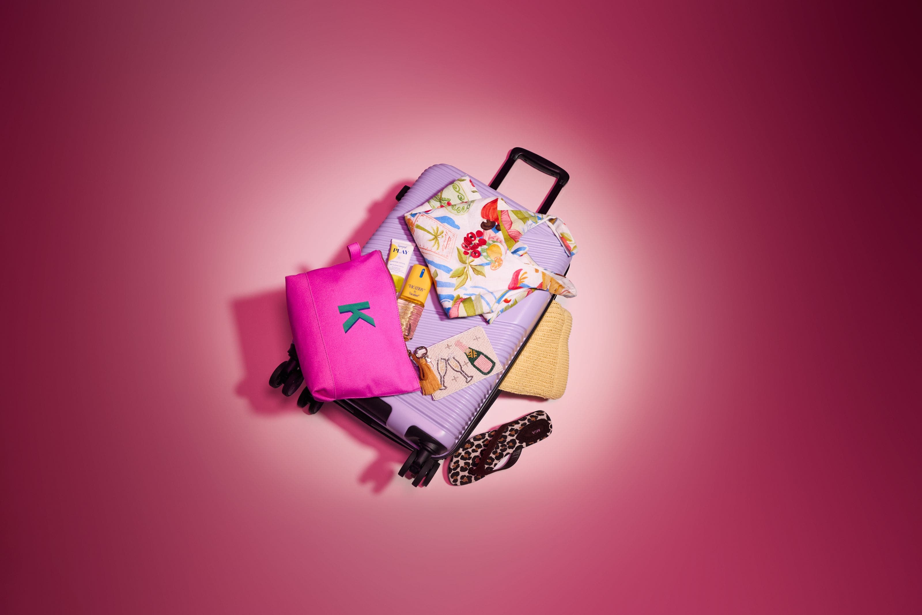 Lavender suitcase with pink pouch, sunscreen, tropical top, straw hat, and leopard flip-flop.