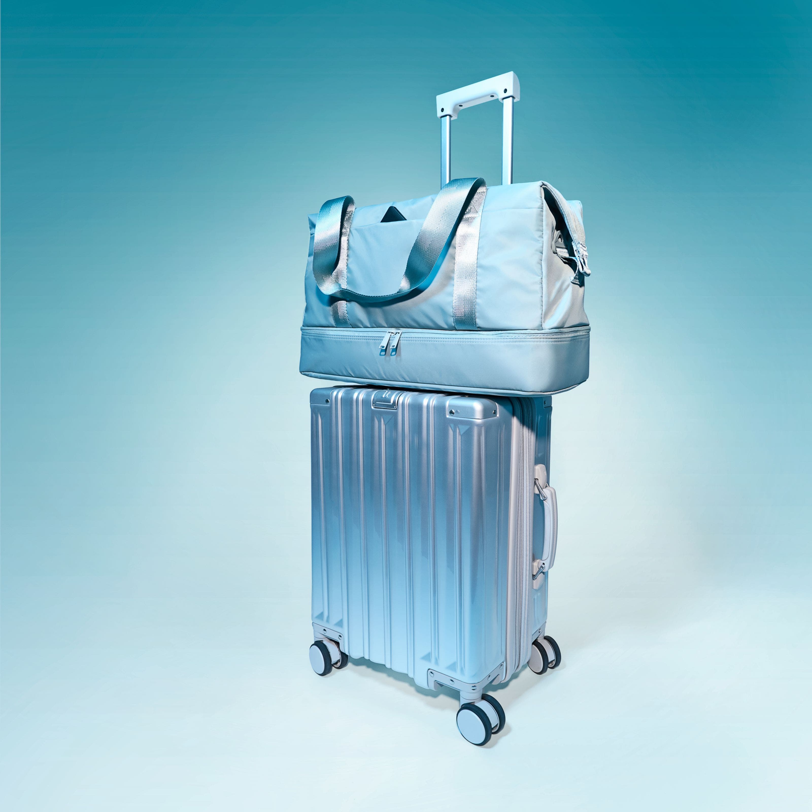 A metallic silver hard‑shell spinner suitcase with a telescoping handle, topped with a matching duffel bag with a trolley sleeve and shoulder straps.