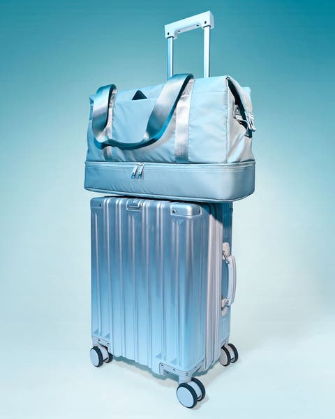A metallic silver hard‑shell spinner suitcase with a telescoping handle, topped with a matching duffel bag with a trolley sleeve and shoulder straps.