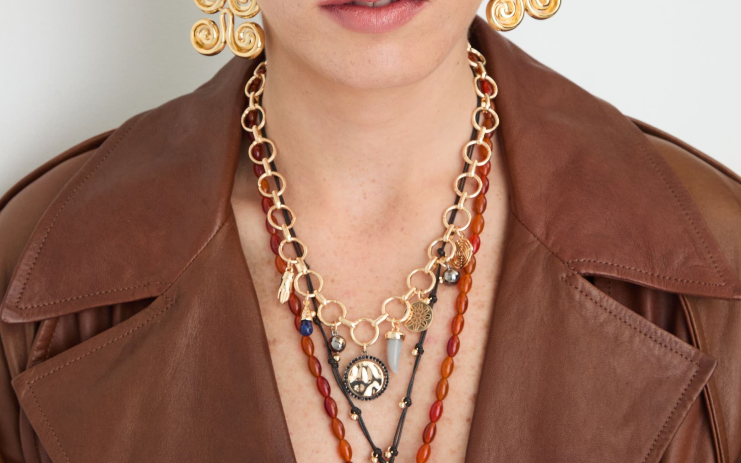 A woman wearing several necklaces and a pair of gold earrings.