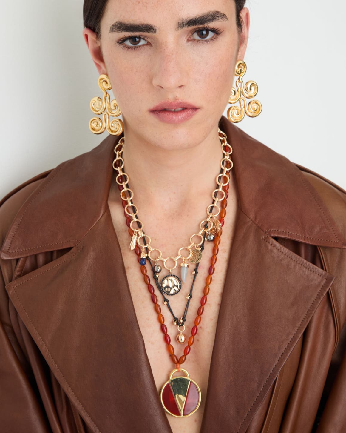 A woman wearing several necklaces and a pair of gold earrings.