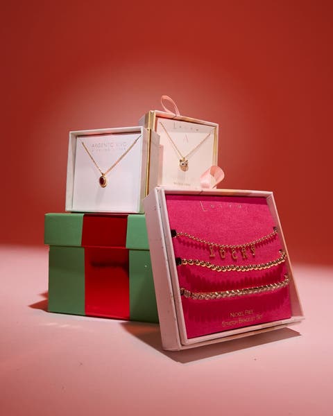Gold necklaces and a stretch bracelet set stacked on a green gift box.