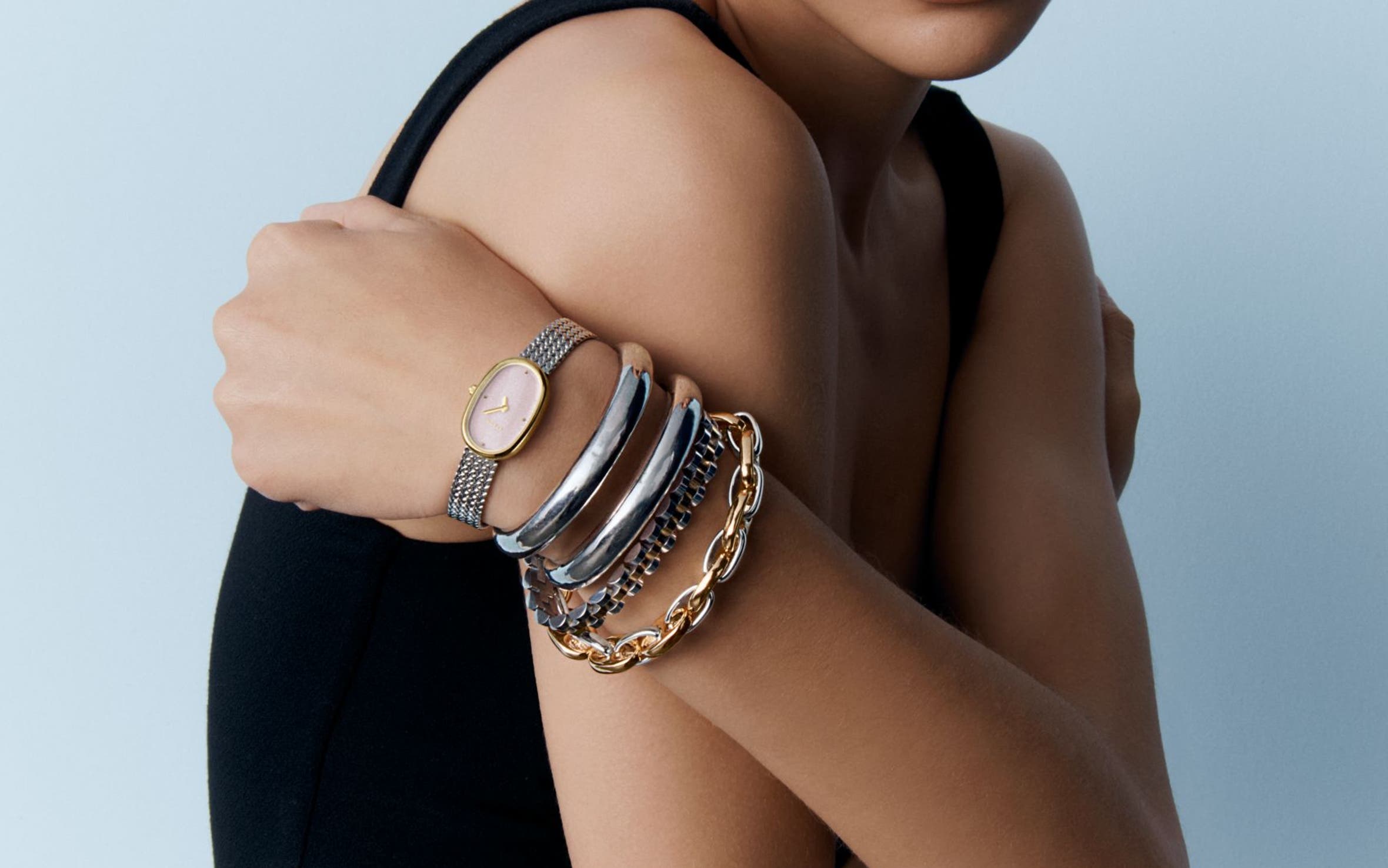 A woman wearing stacked silver bangles, silver watch and chunky gold chain bracelets.