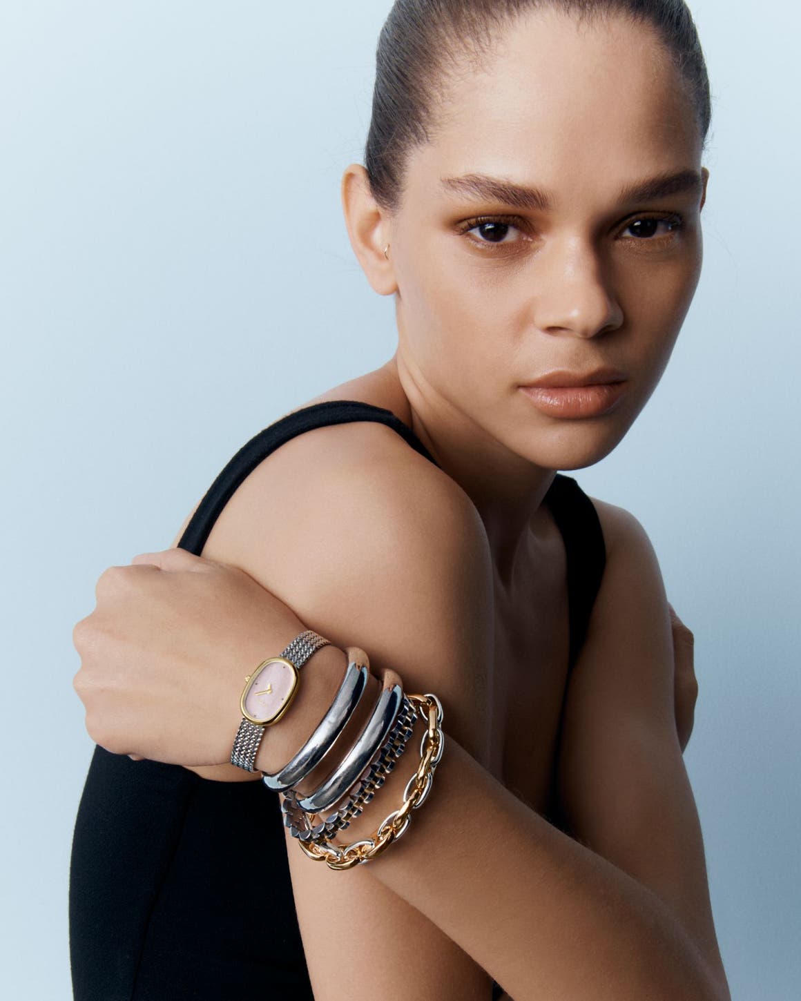 A woman wearing stacked silver bangles, silver watch and chunky gold chain bracelets.