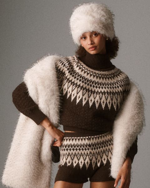 A woman wearing a fair isle sweater with white fuzzy hat and scarf.