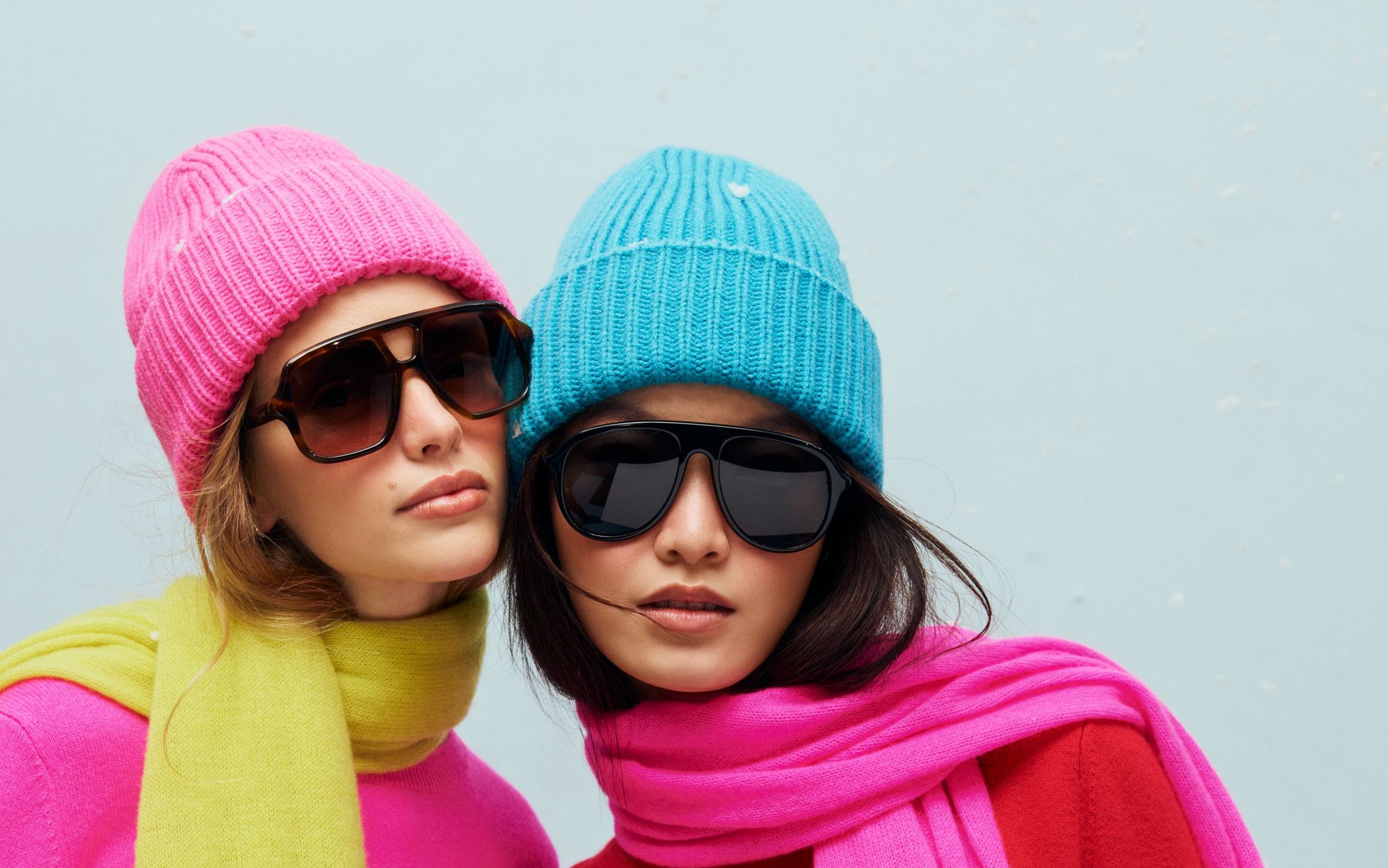 Two women wearing knit hats, sweaters and scarves.