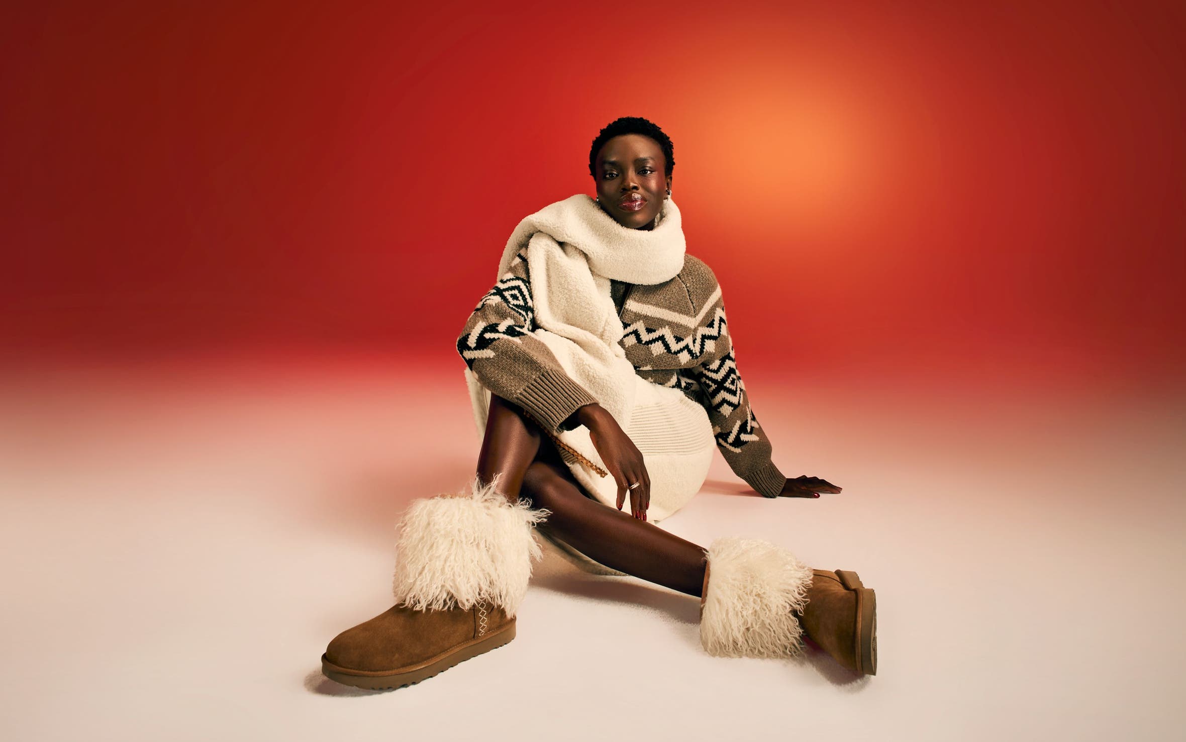 A woman wearing a cozy scarf, sweater, skirt and boots.