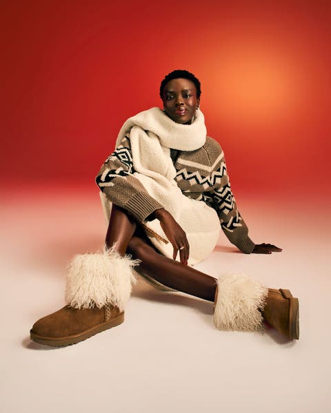 Model wearing a Fair Isle sweater, cream oversized scarf, white midi skirt, and chestnut UGG boots with shearling cuff trim.