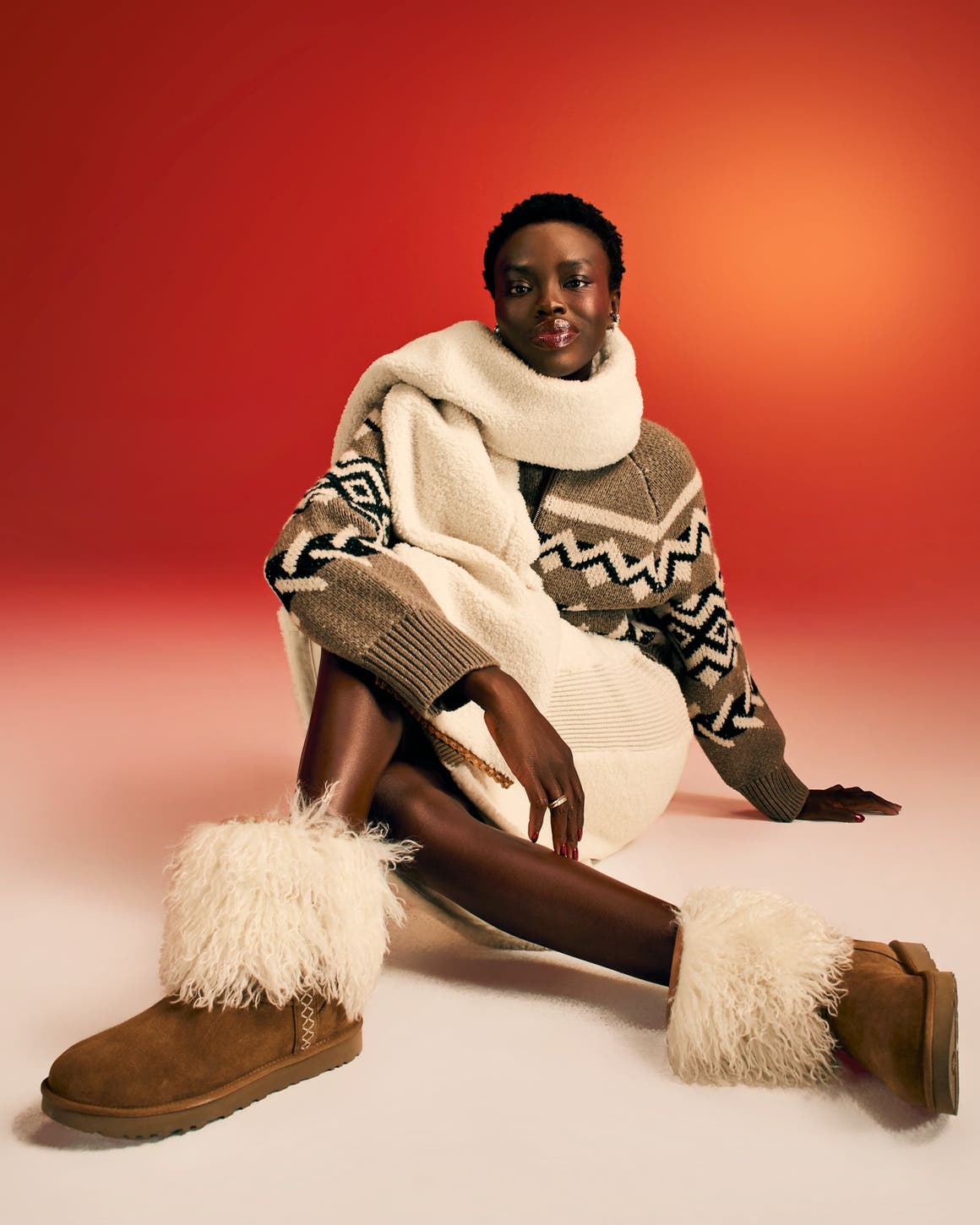 A woman wearing a cozy scarf, sweater, skirt and boots.