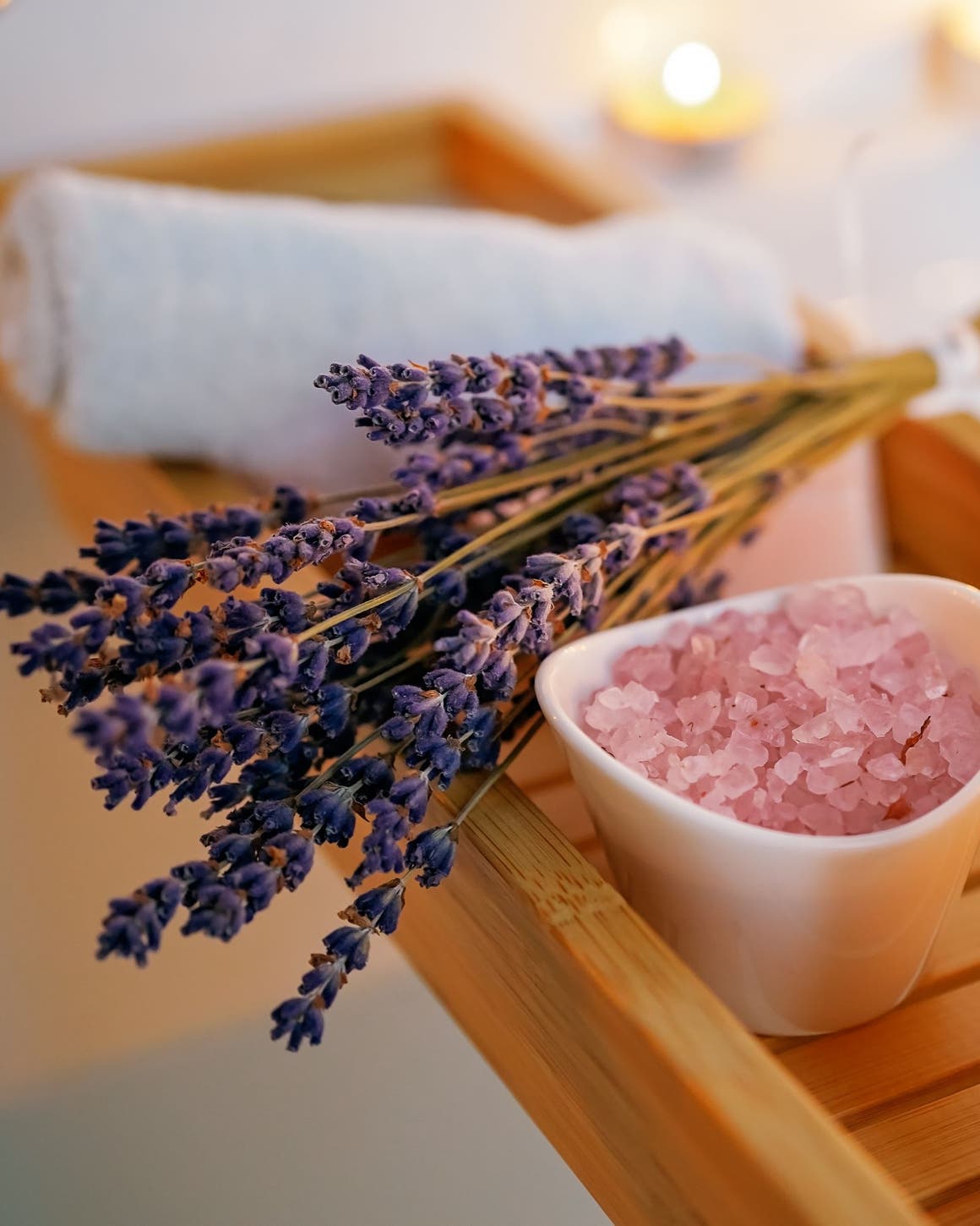 A wooden bathtub tray with lavender, bath salts and a candle.