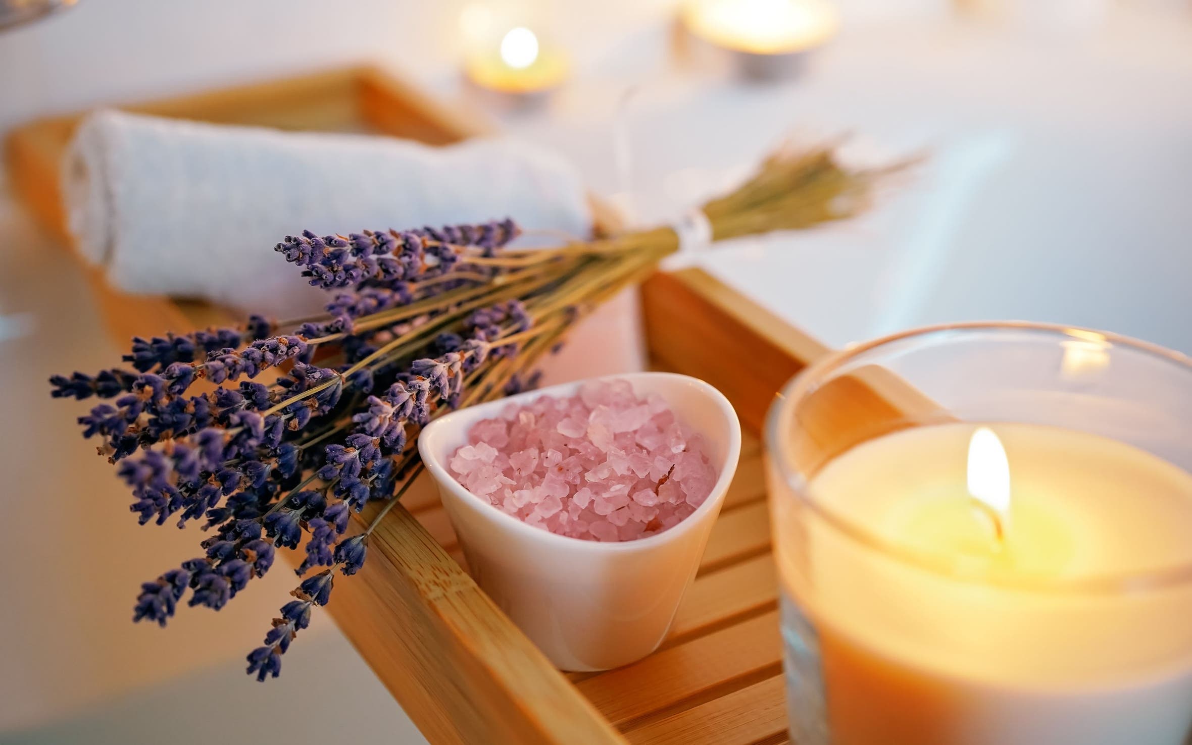A wooden bathtub tray with lavender, bath salts and a candle.