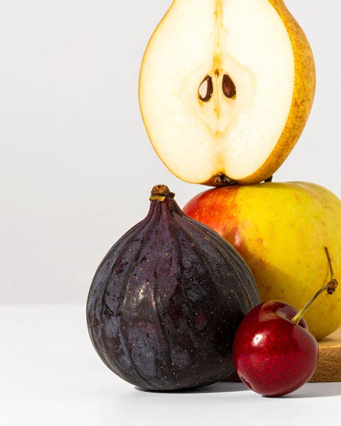 Still life arrangement of a fig, cherry, and apple with a halved pear on a white background
