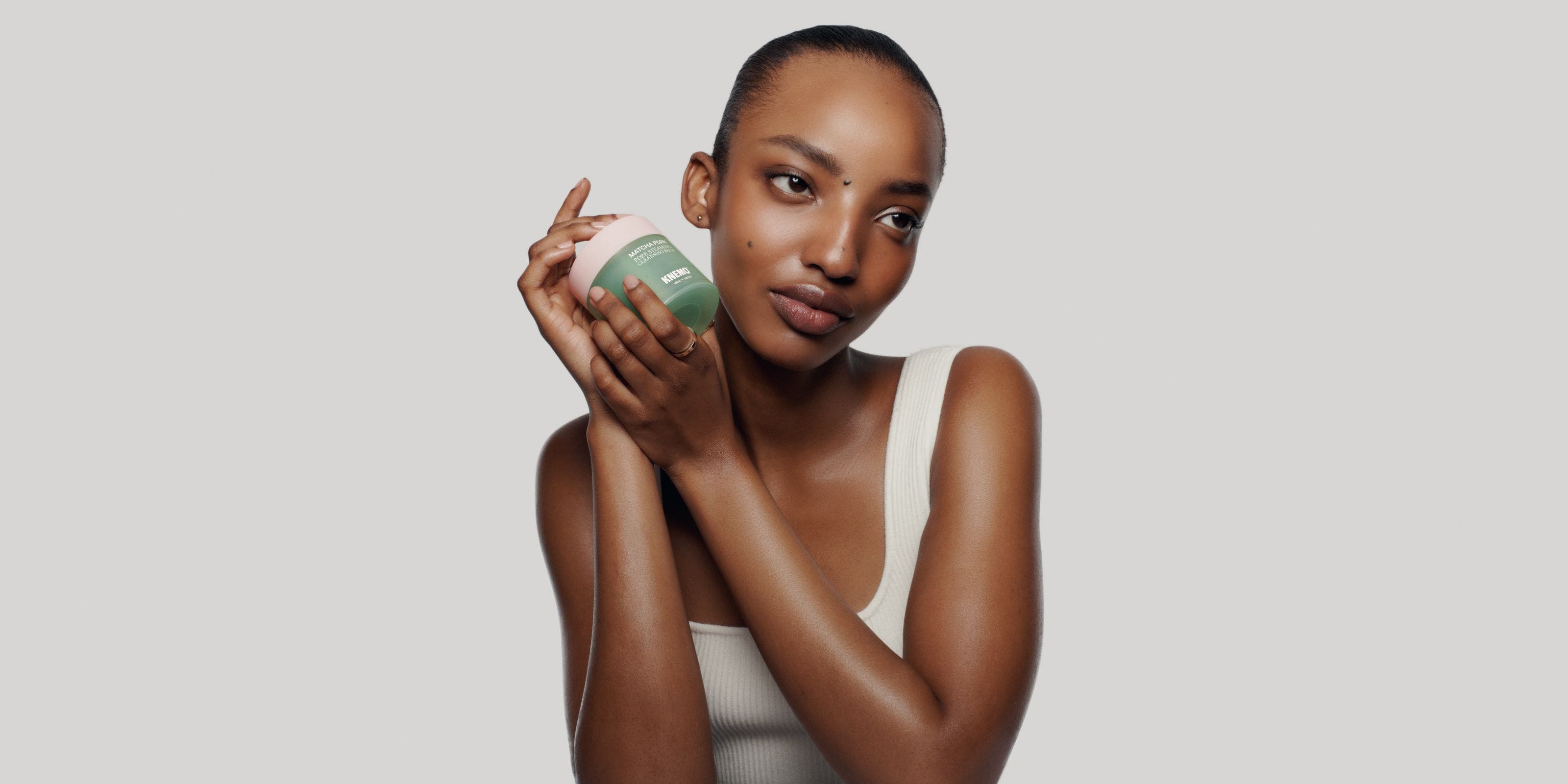 A woman with glowy skin holds a cleansing balm.