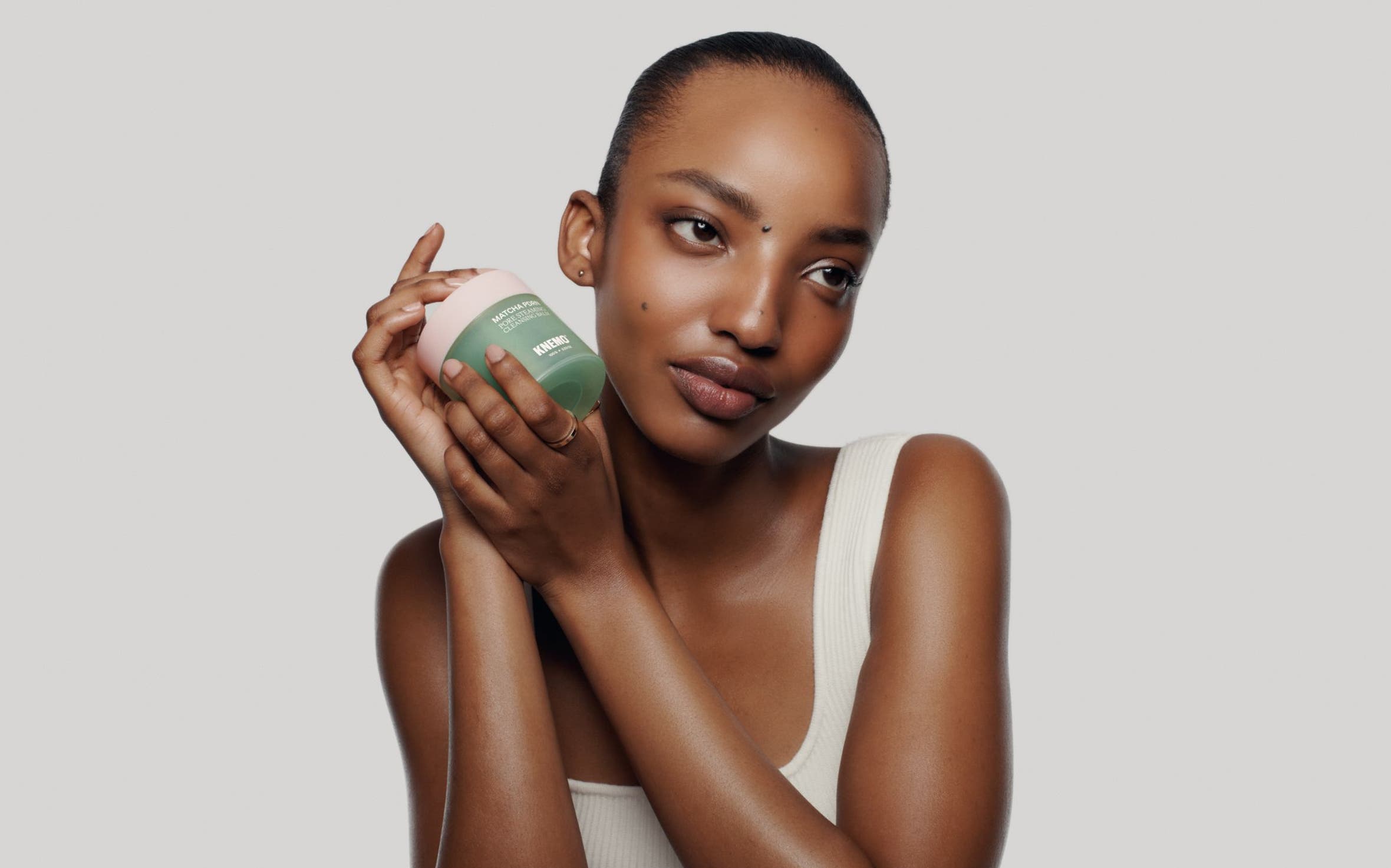 A woman with glowy skin holds a cleansing balm.