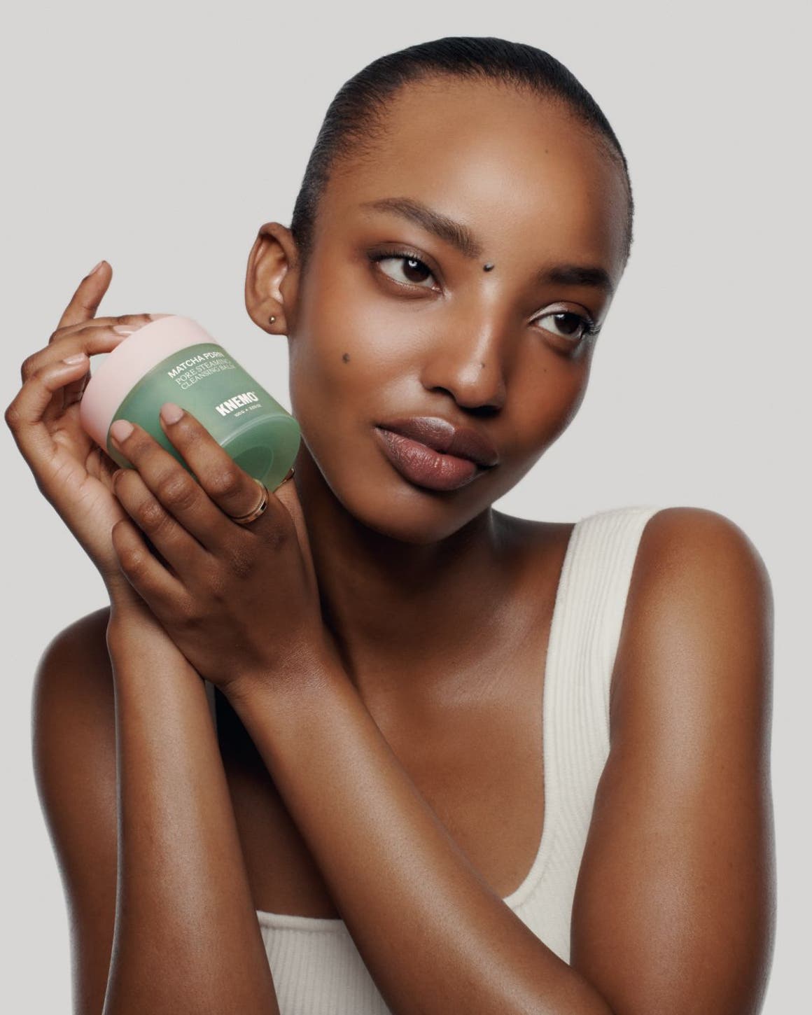 A woman with glowy skin holds a cleansing balm.
