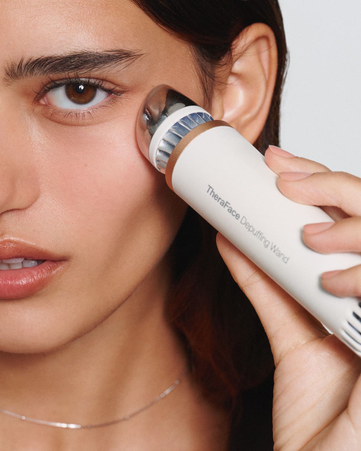 A woman using a depuffing skin care device.