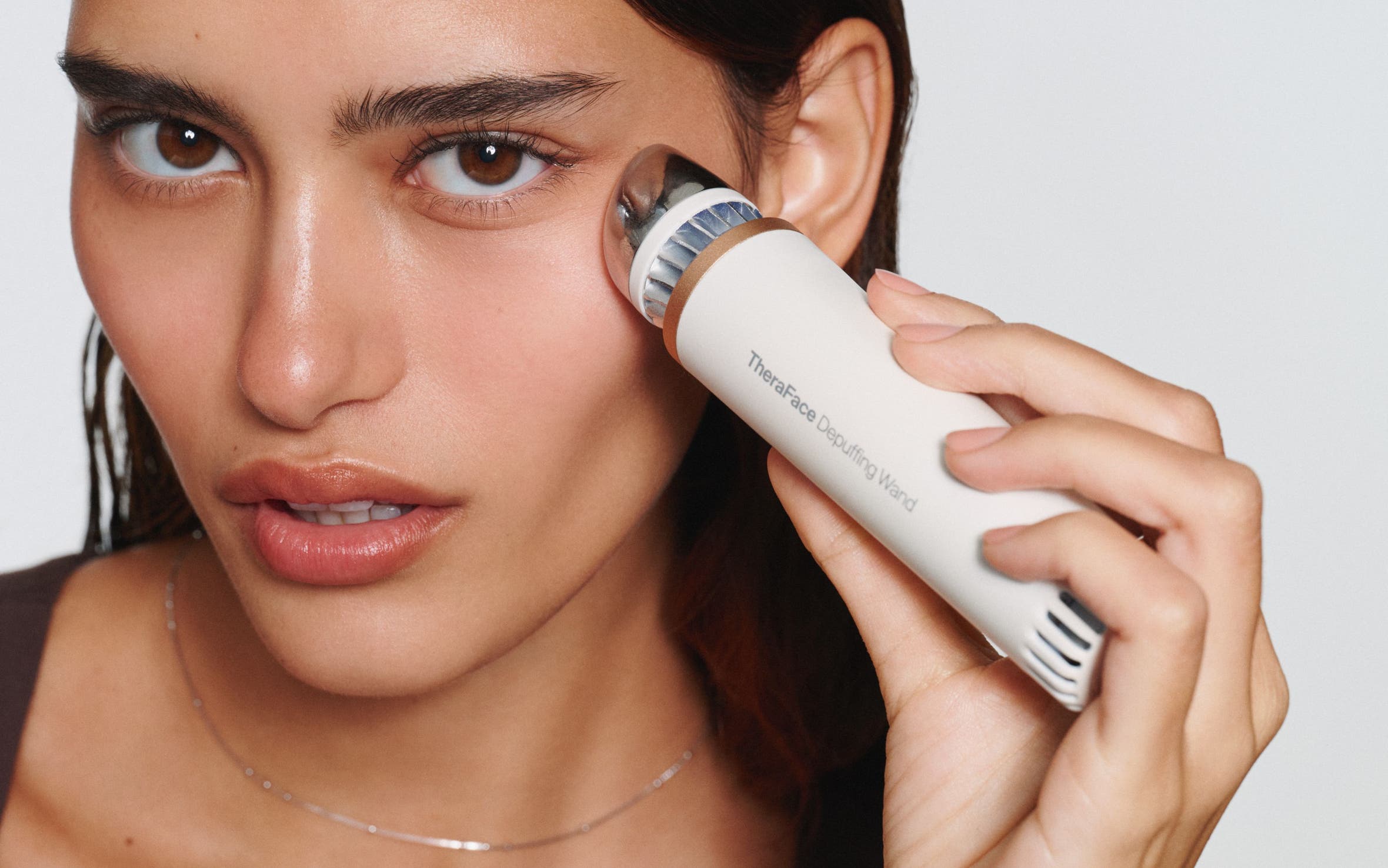 A woman using a depuffing skin care device.