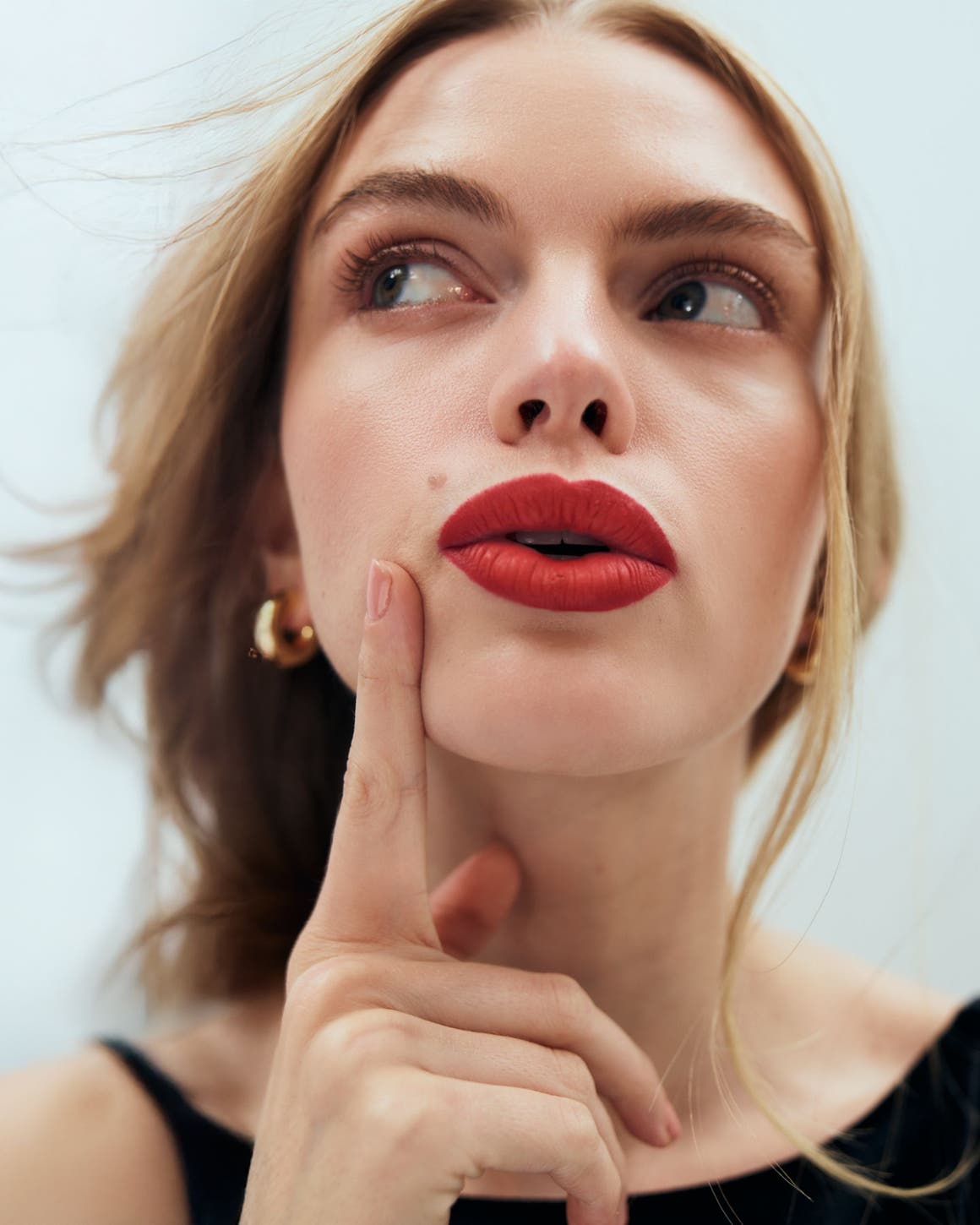 A blonde model with red lipstick and gold hoop earrings.