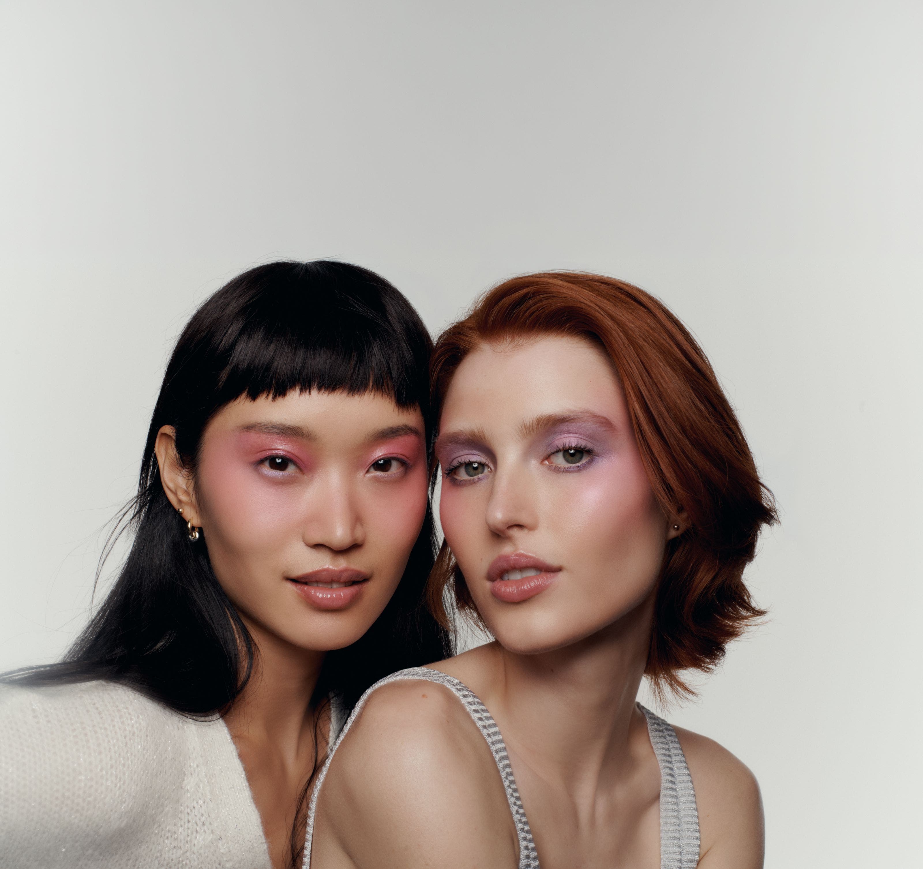 Two women with soft-glam makeup looks featuring shimmery pink and mauve eyeshadow, close-up beauty portrait.