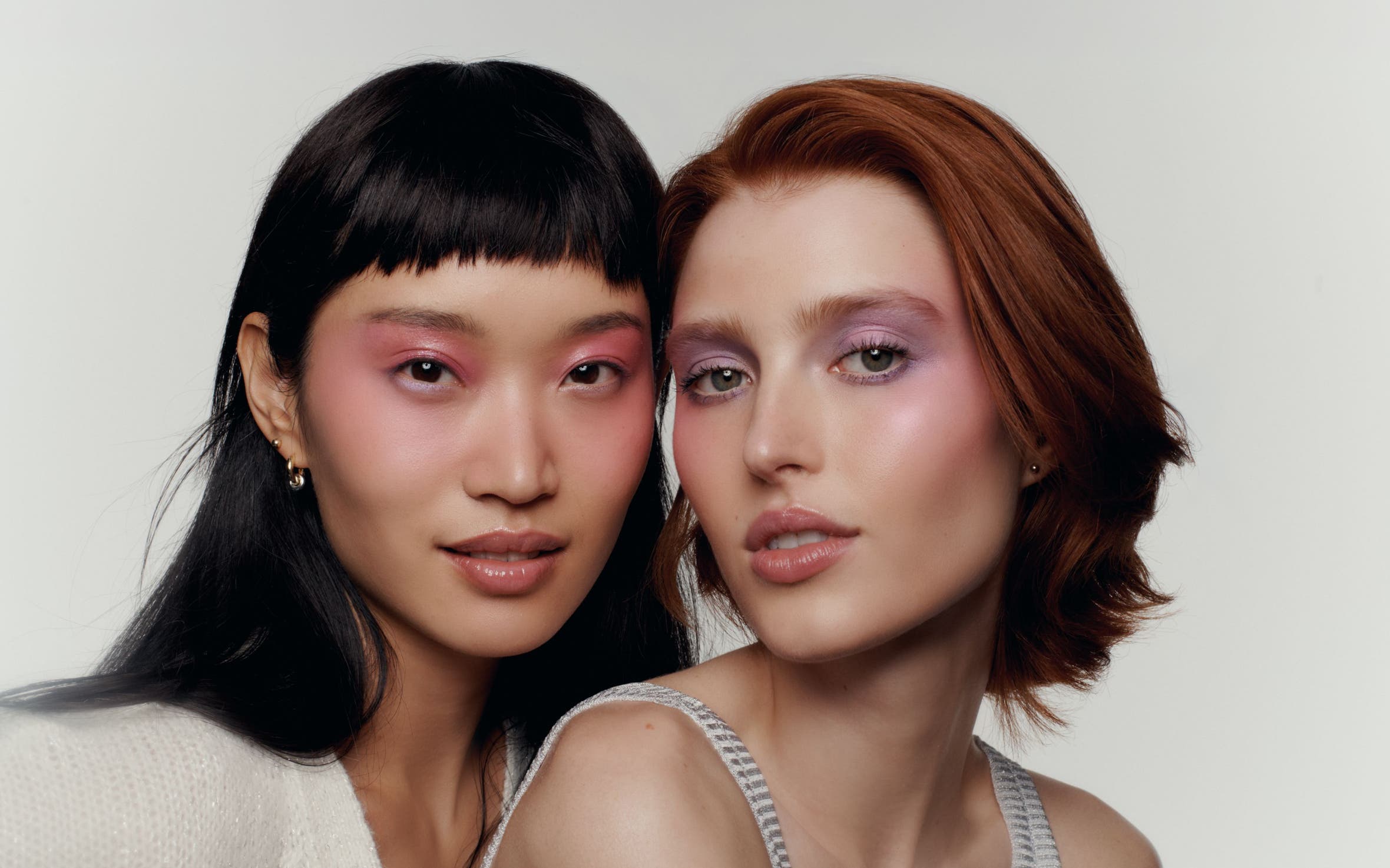 Two women with soft-glam makeup looks featuring shimmery pink and mauve eyeshadow, close-up beauty portrait.