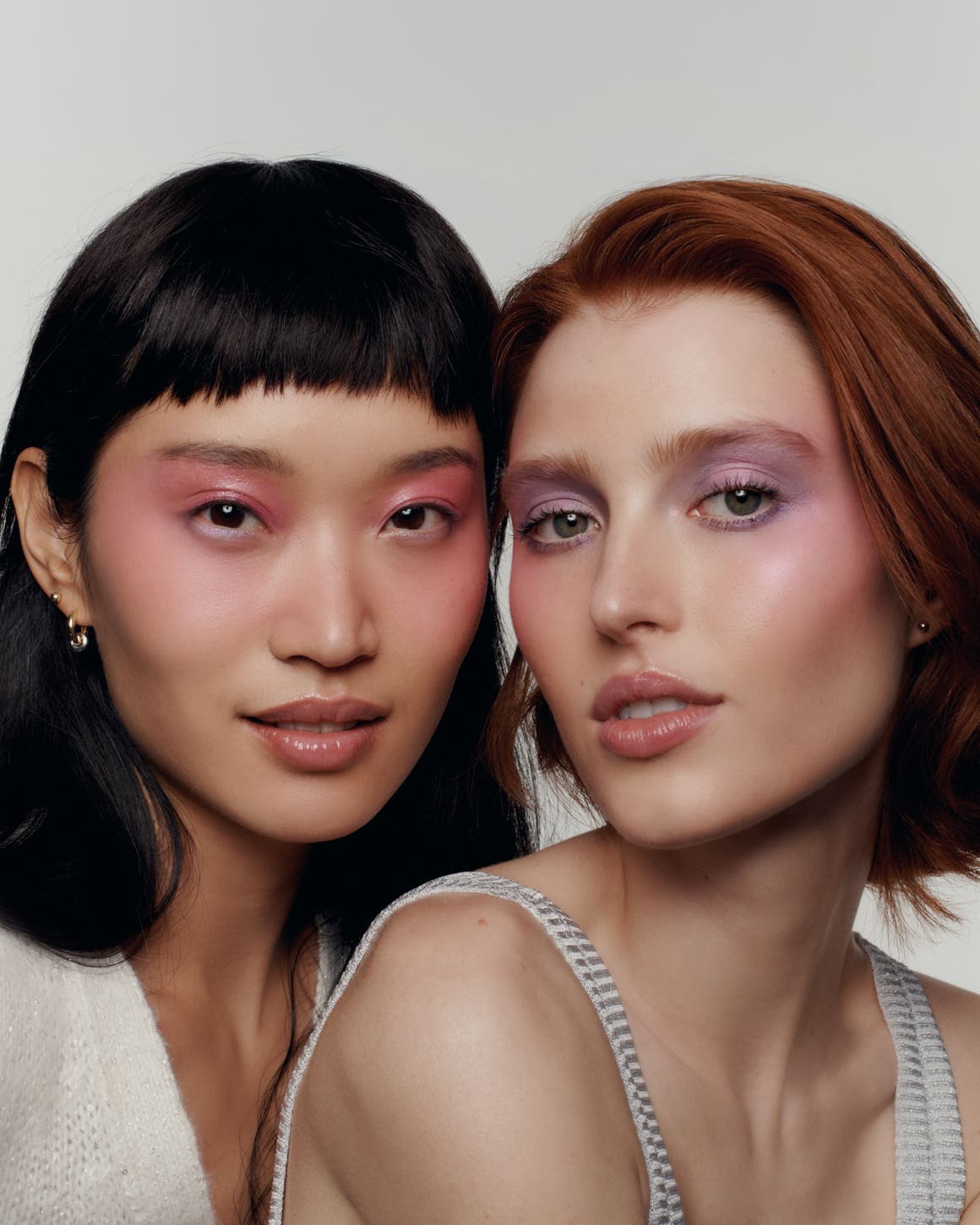 Two women with soft-glam makeup looks featuring shimmery pink and mauve eyeshadow, close-up beauty portrait.