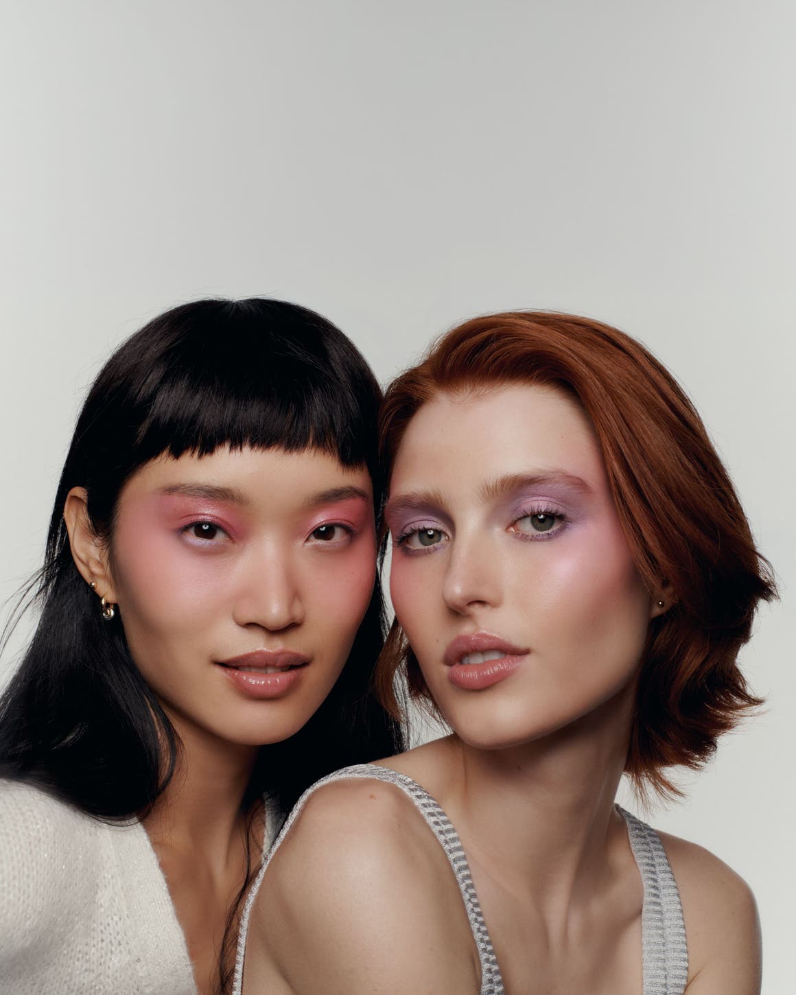 Two women with soft-glam makeup looks featuring shimmery pink and mauve eyeshadow, close-up beauty portrait.