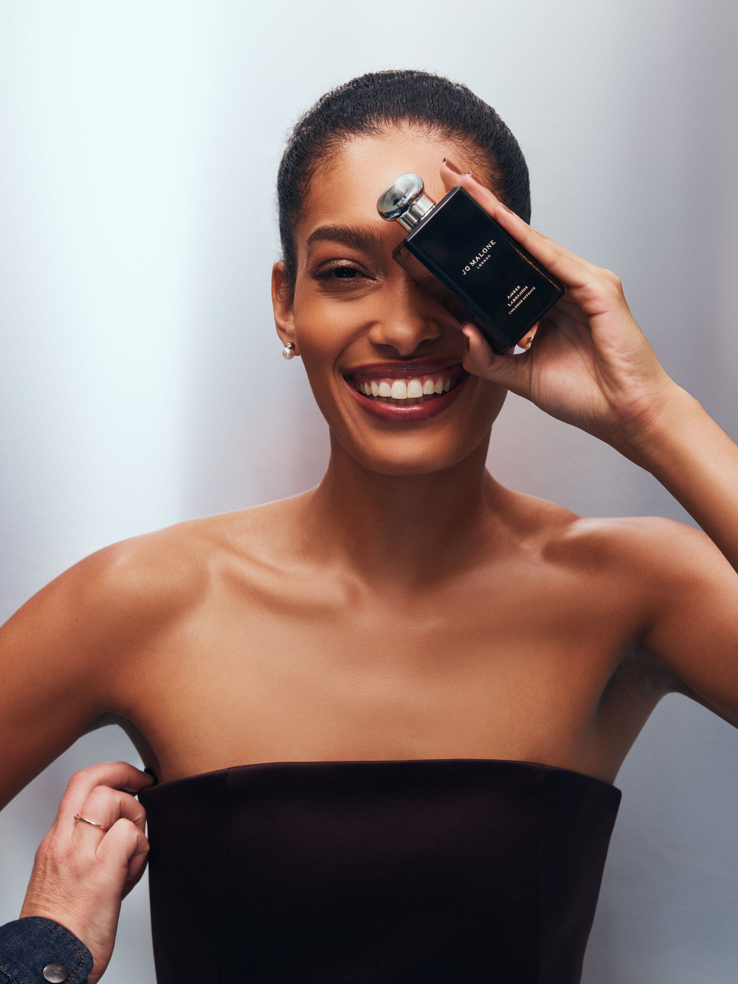 A model holding a Jo Malone perfume bottle in front of her face.