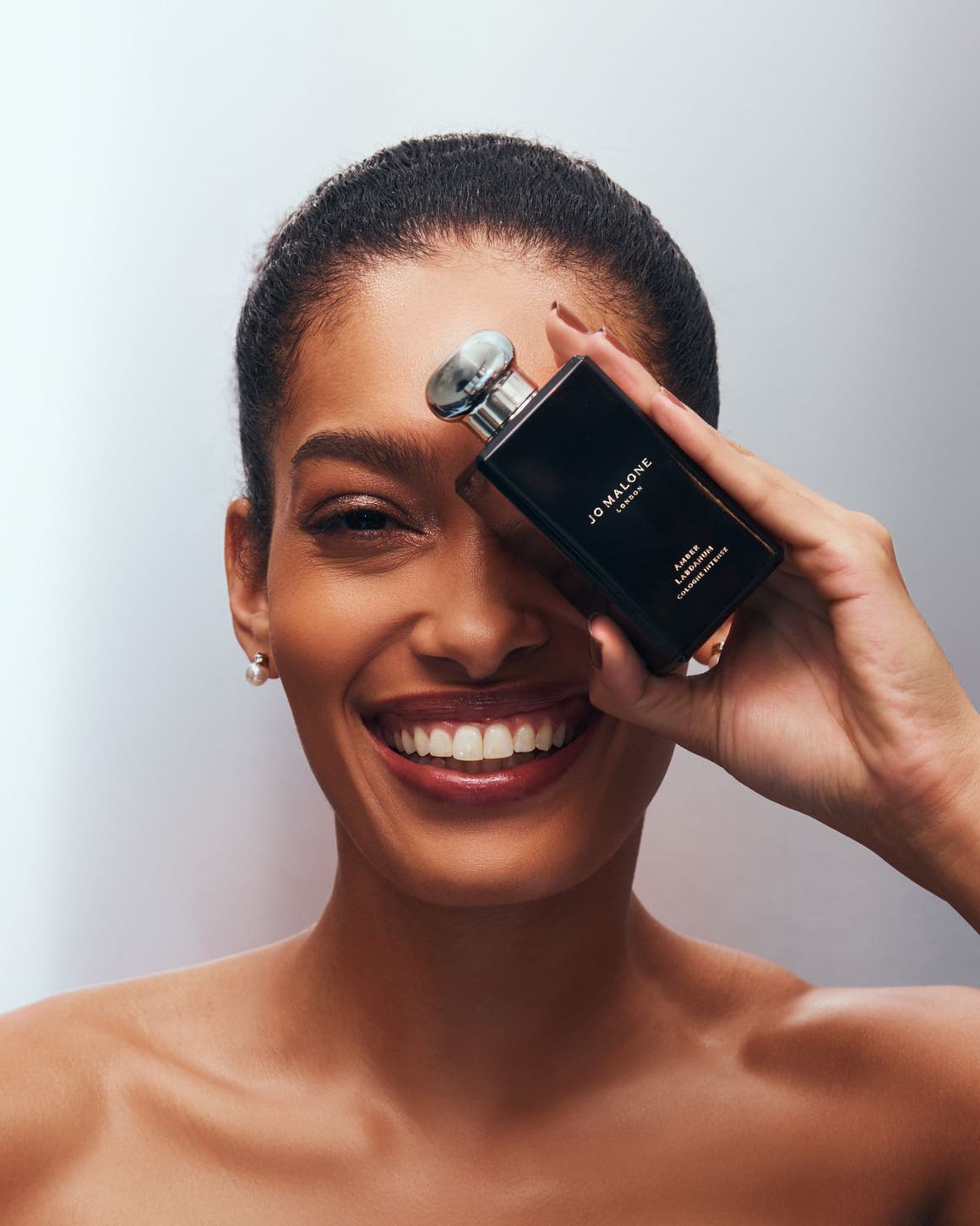 A model holding a Jo Malone perfume bottle in front of her face.