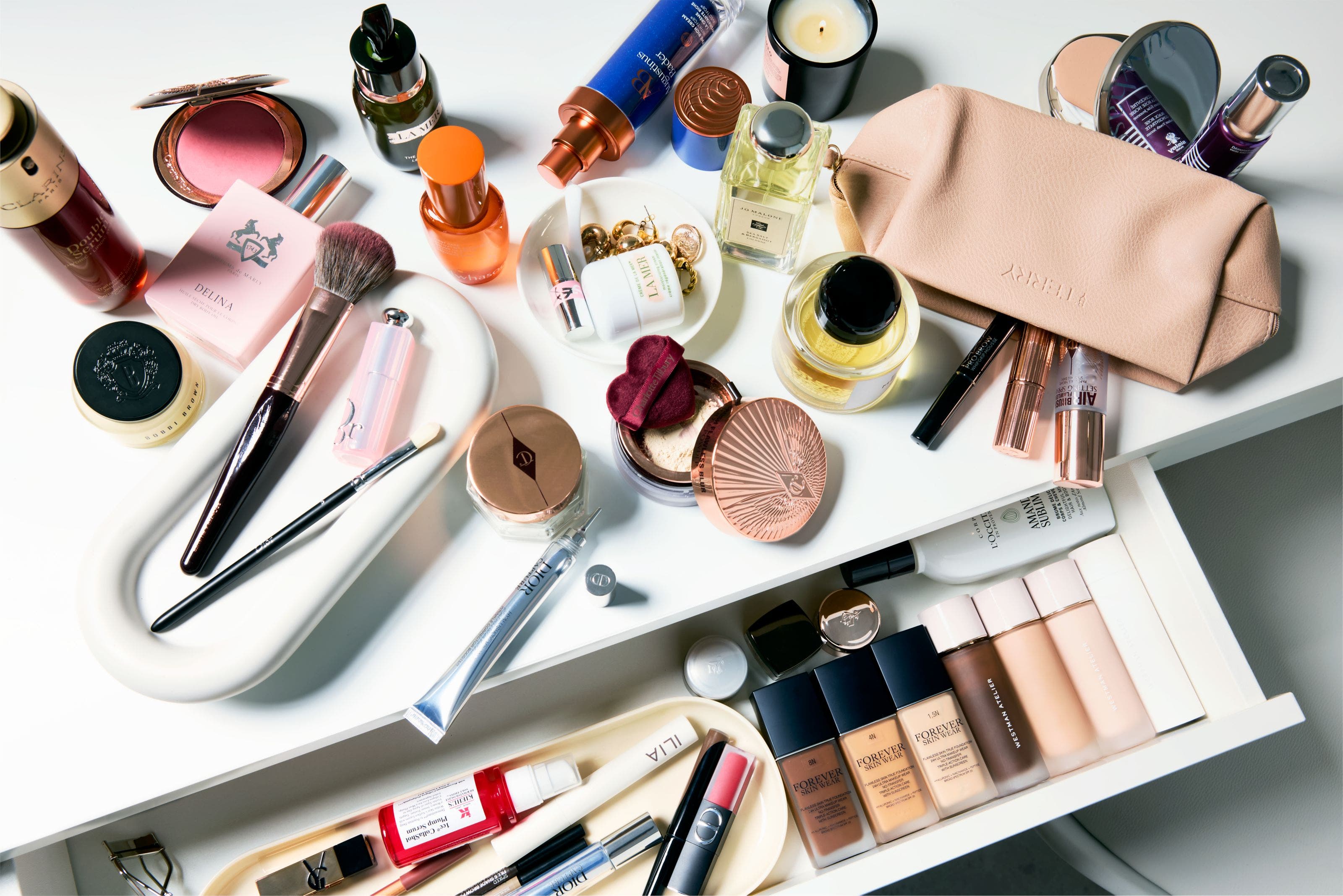 A counter and drawer full of makeup, skin care, fragrance and beauty tools. 