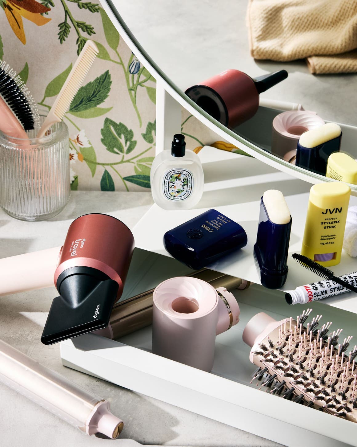 Hair care products, hair tools, mascara and perfume on a vanity.