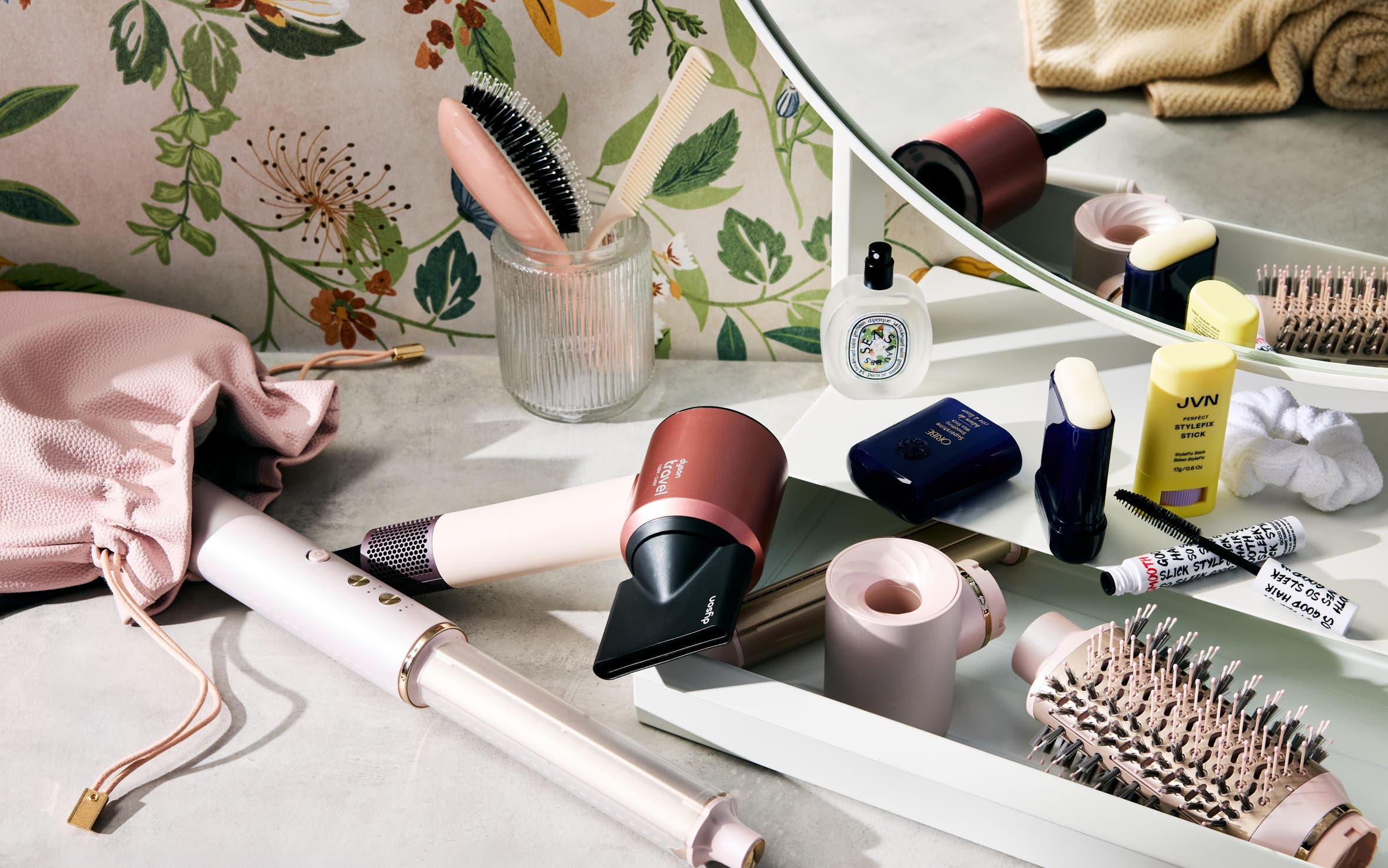 Hair care products, hair tools, mascara and perfume on a vanity.