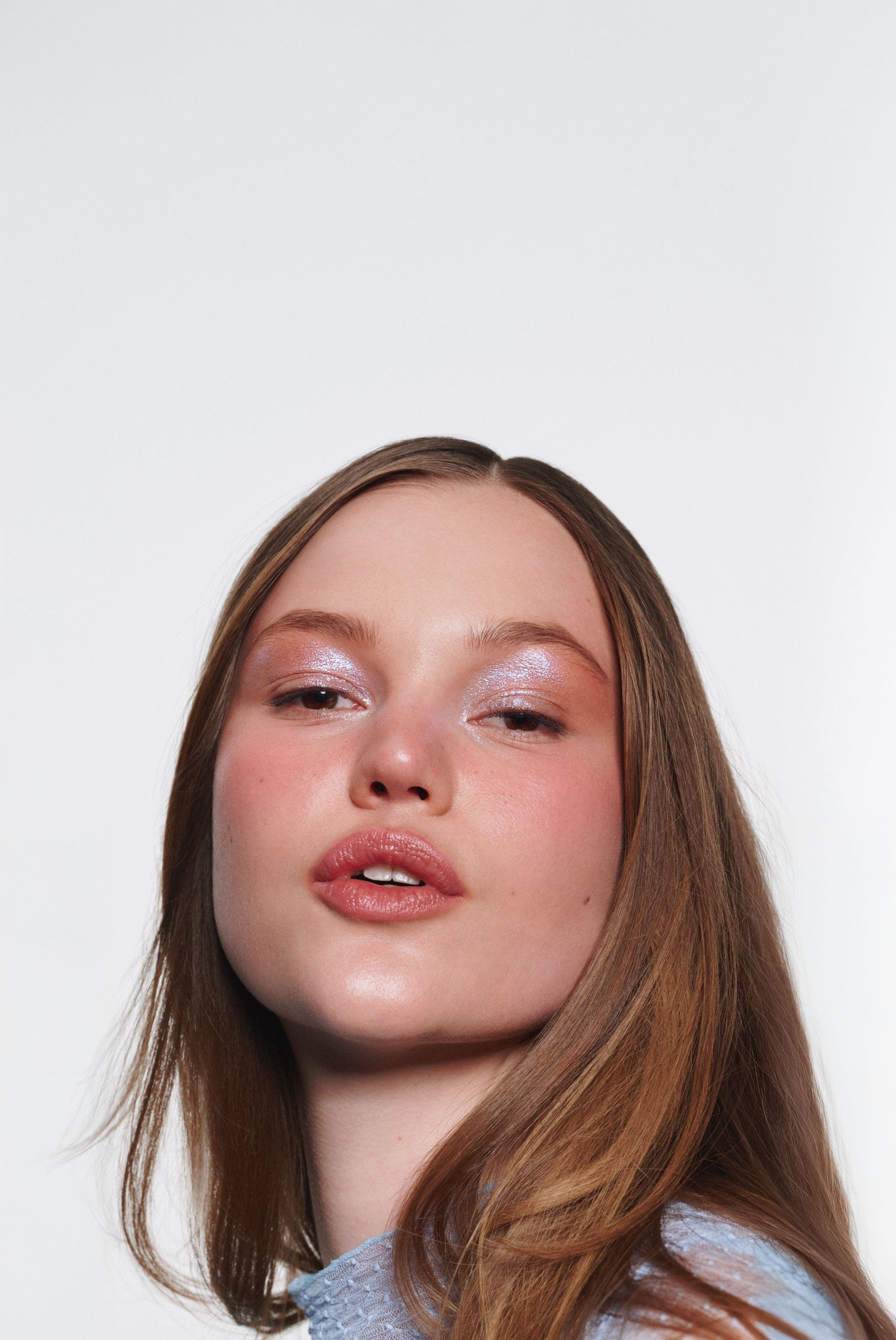 A woman wearing iridescent pink eyeshadow and glossy pink lipstick.