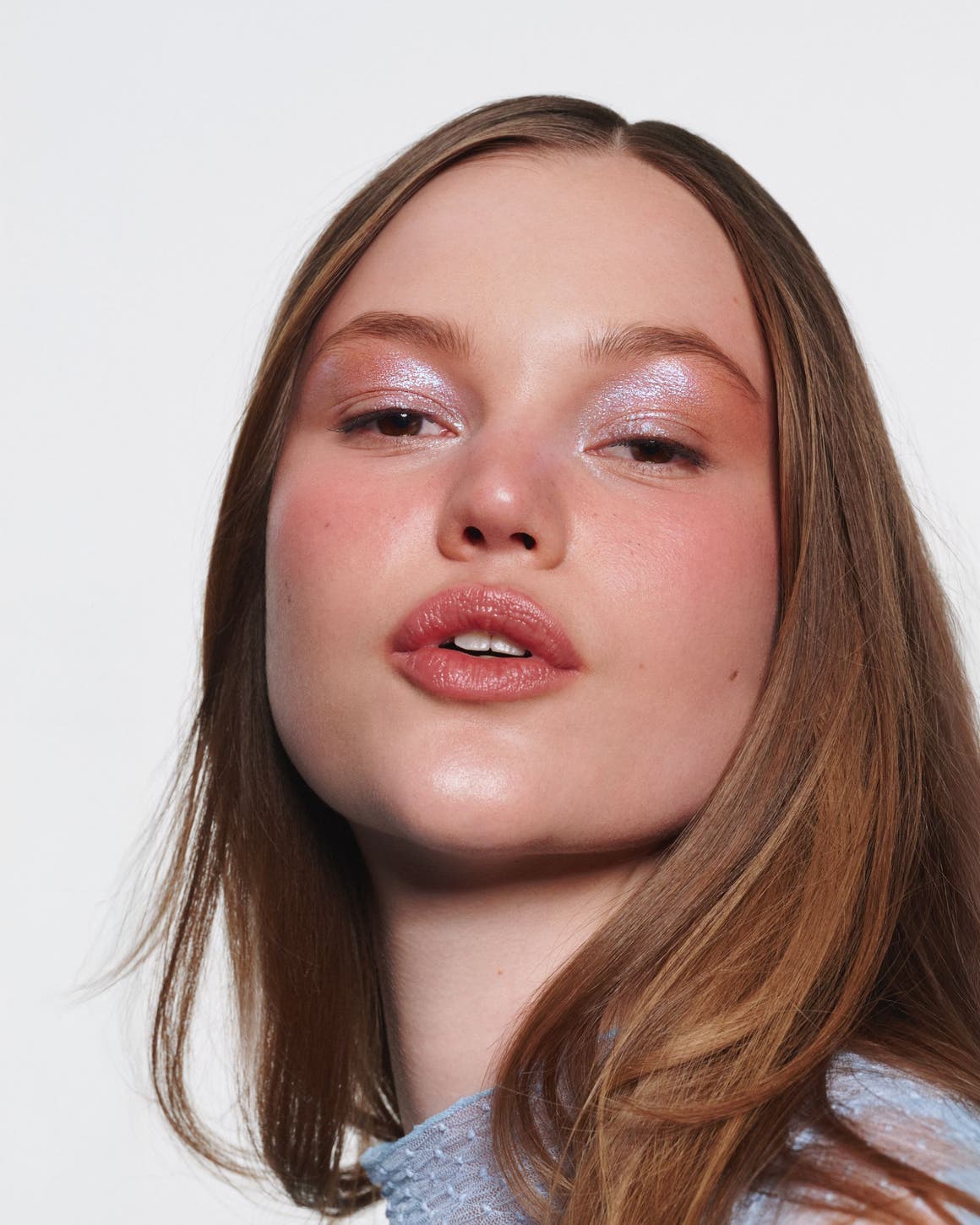 A woman wearing iridescent pink eyeshadow and glossy pink lipstick.