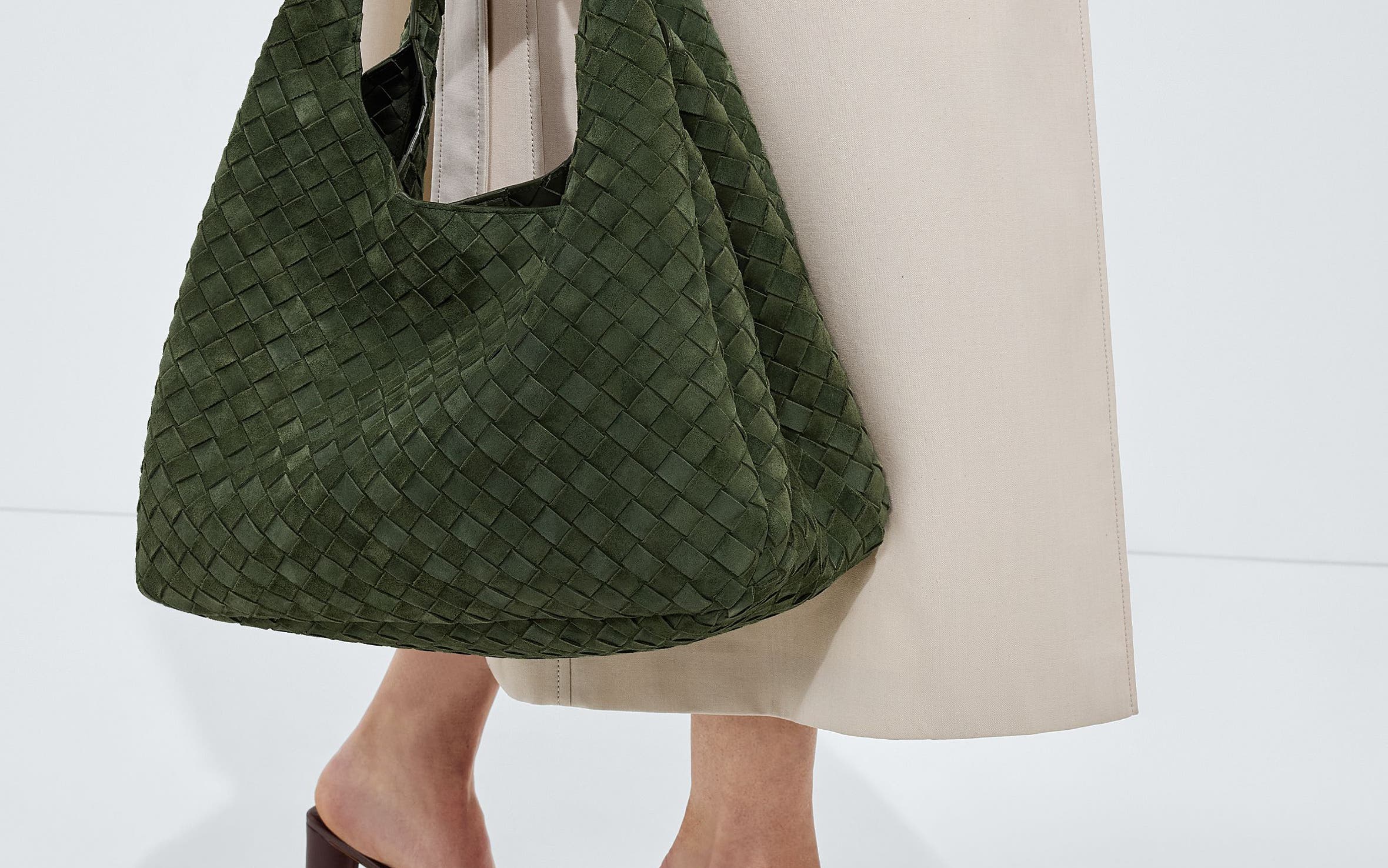 A woman carrying a woven olive shoulder bag.