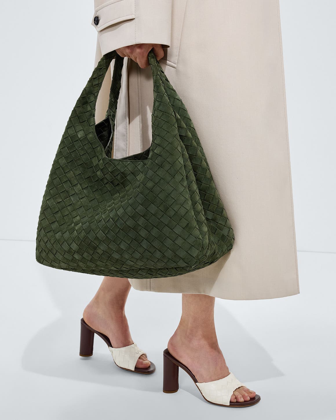 A woman carrying a woven olive shoulder bag.