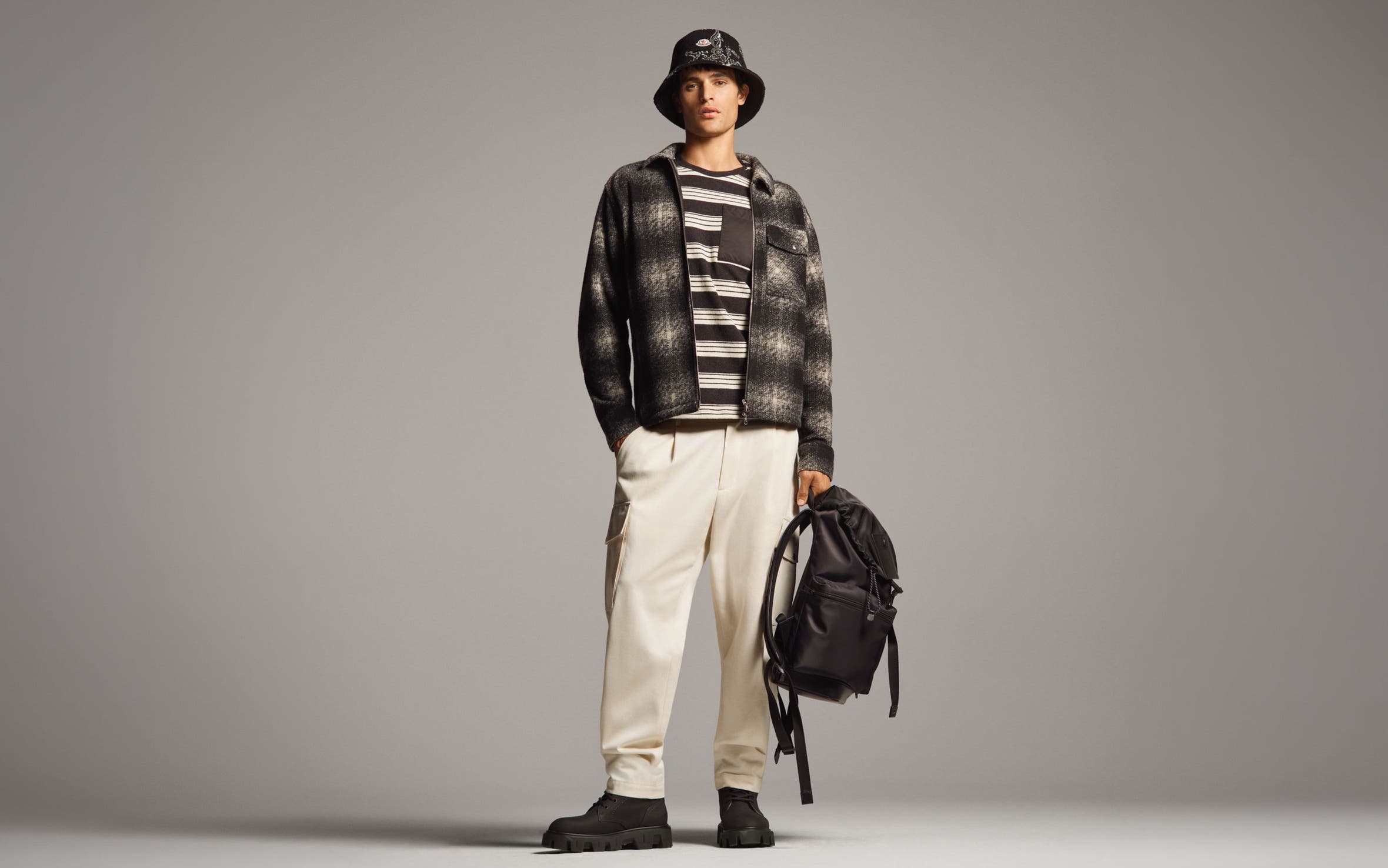 A man in a plaid jacket, bucket hat, and cream cargo pants.