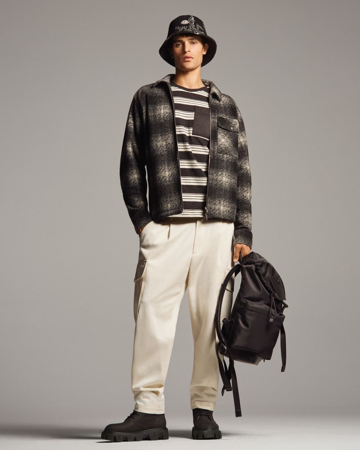 A man in a plaid jacket, bucket hat, and cream cargo pants.