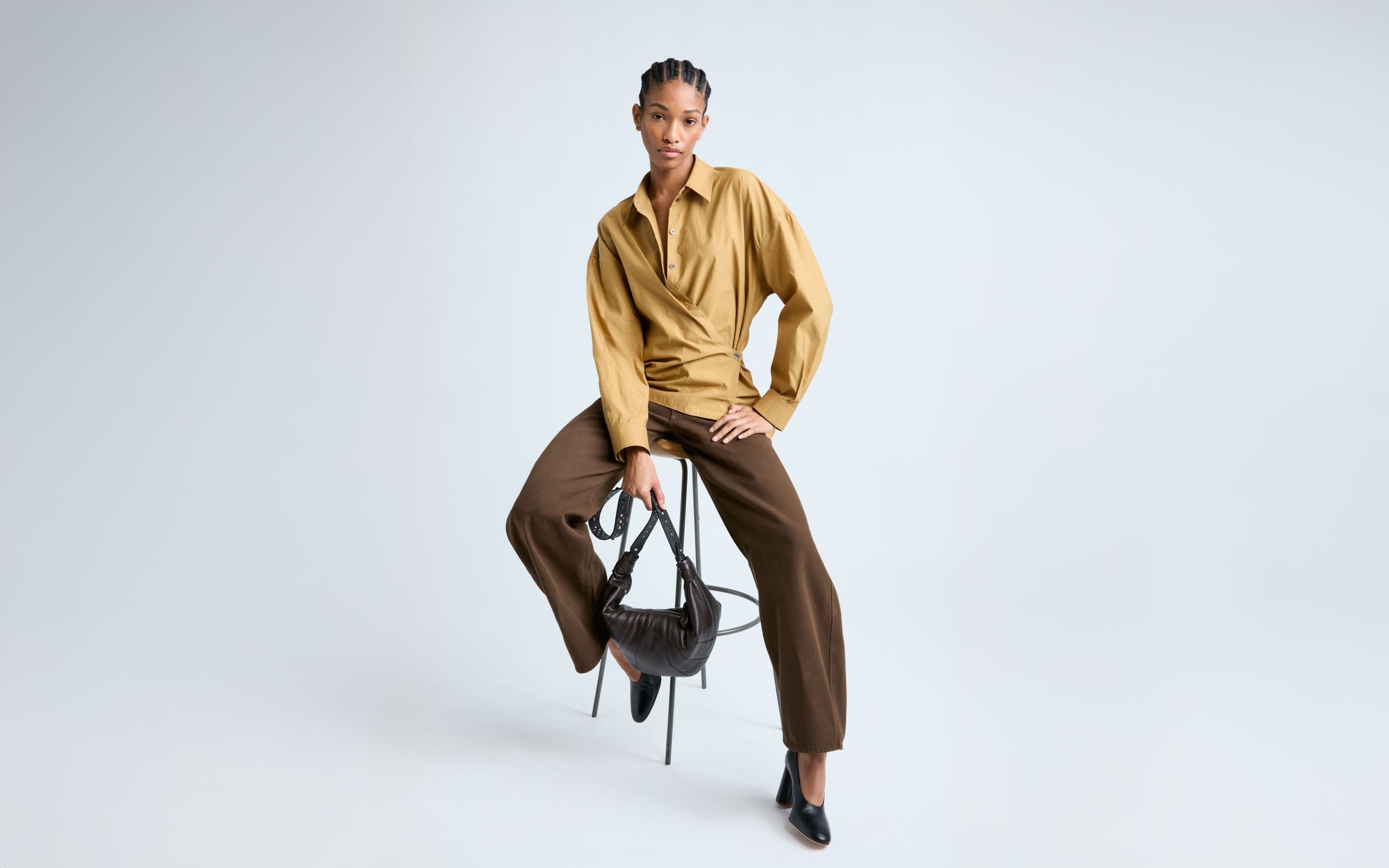 Woman wearing a shirt with wrap detail and trousers in shades of brown. 