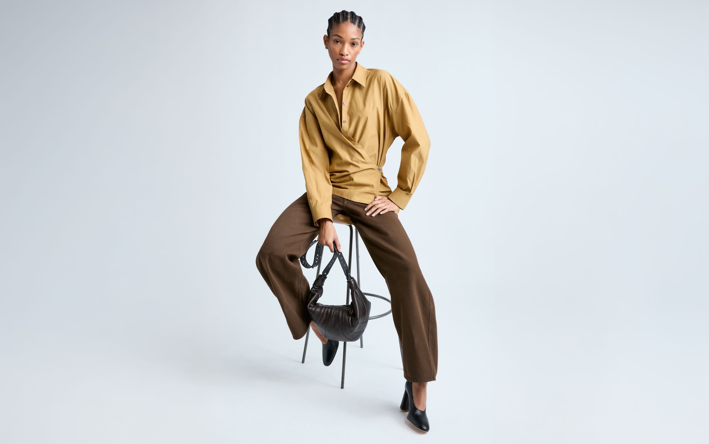 Woman wearing a shirt with wrap detail and trousers in shades of brown.