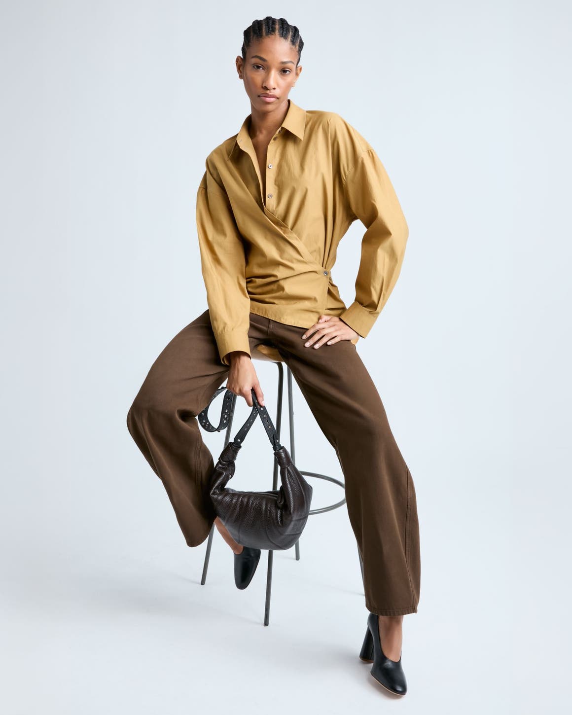 Woman wearing a shirt with wrap detail and trousers in shades of brown.