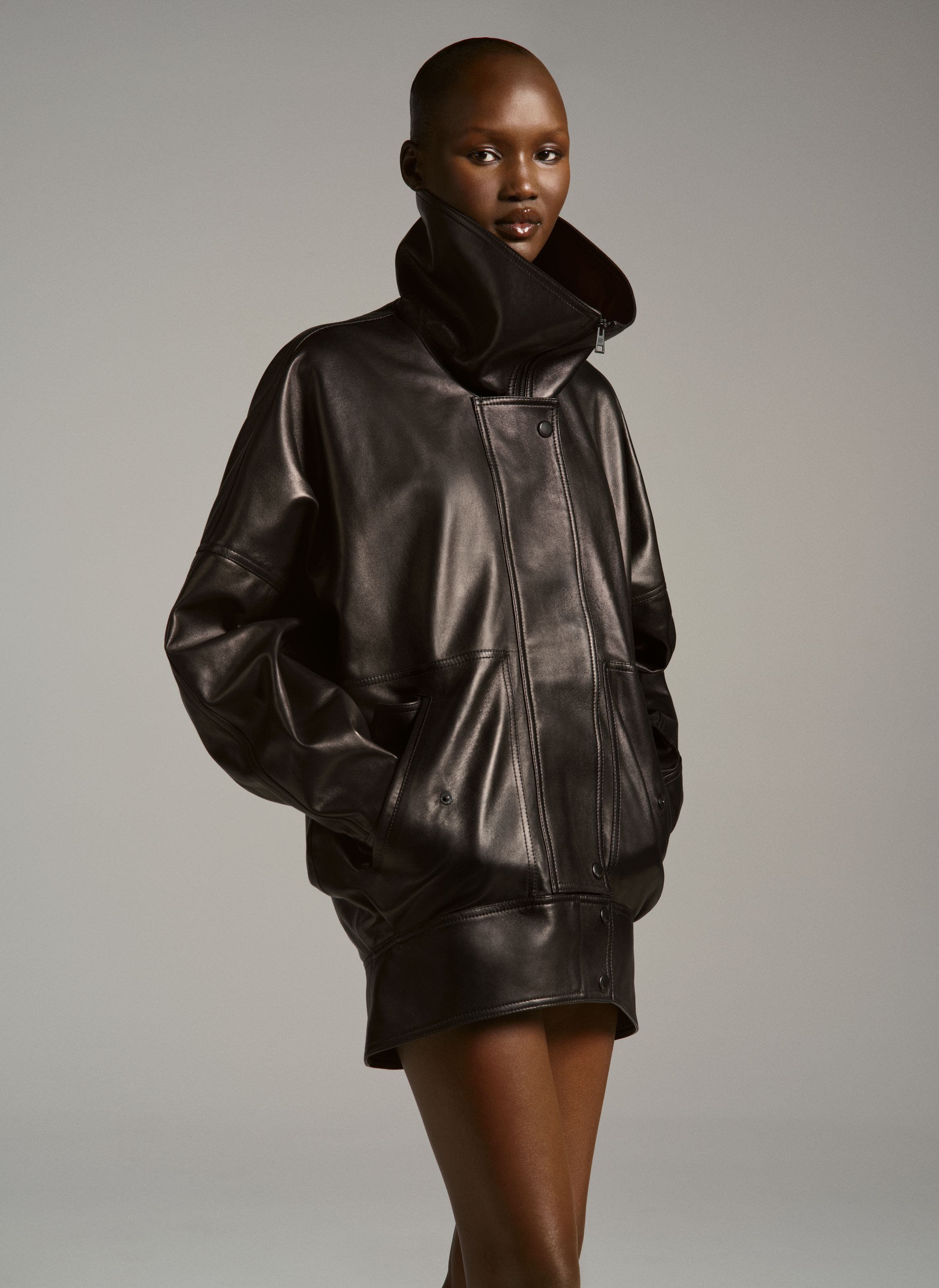 Model wearing an oversized dark leather jacket with dramatic gathered/shearling-trim collar
