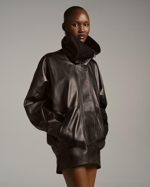 Model wearing an oversized dark leather jacket with dramatic gathered/shearling-trim collar